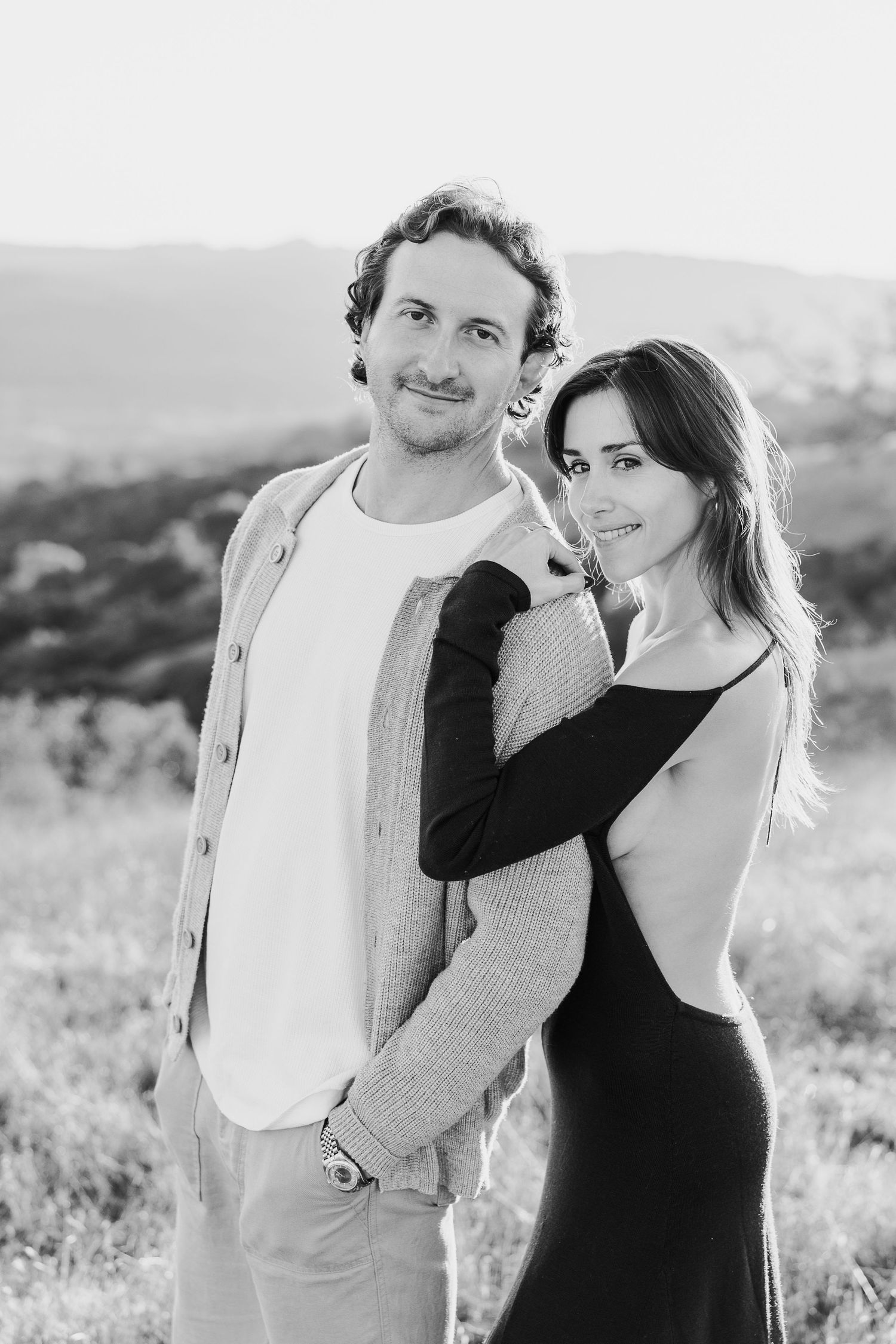 A couple in contrasting black and white outfits pose together in a natural outdoor setting.