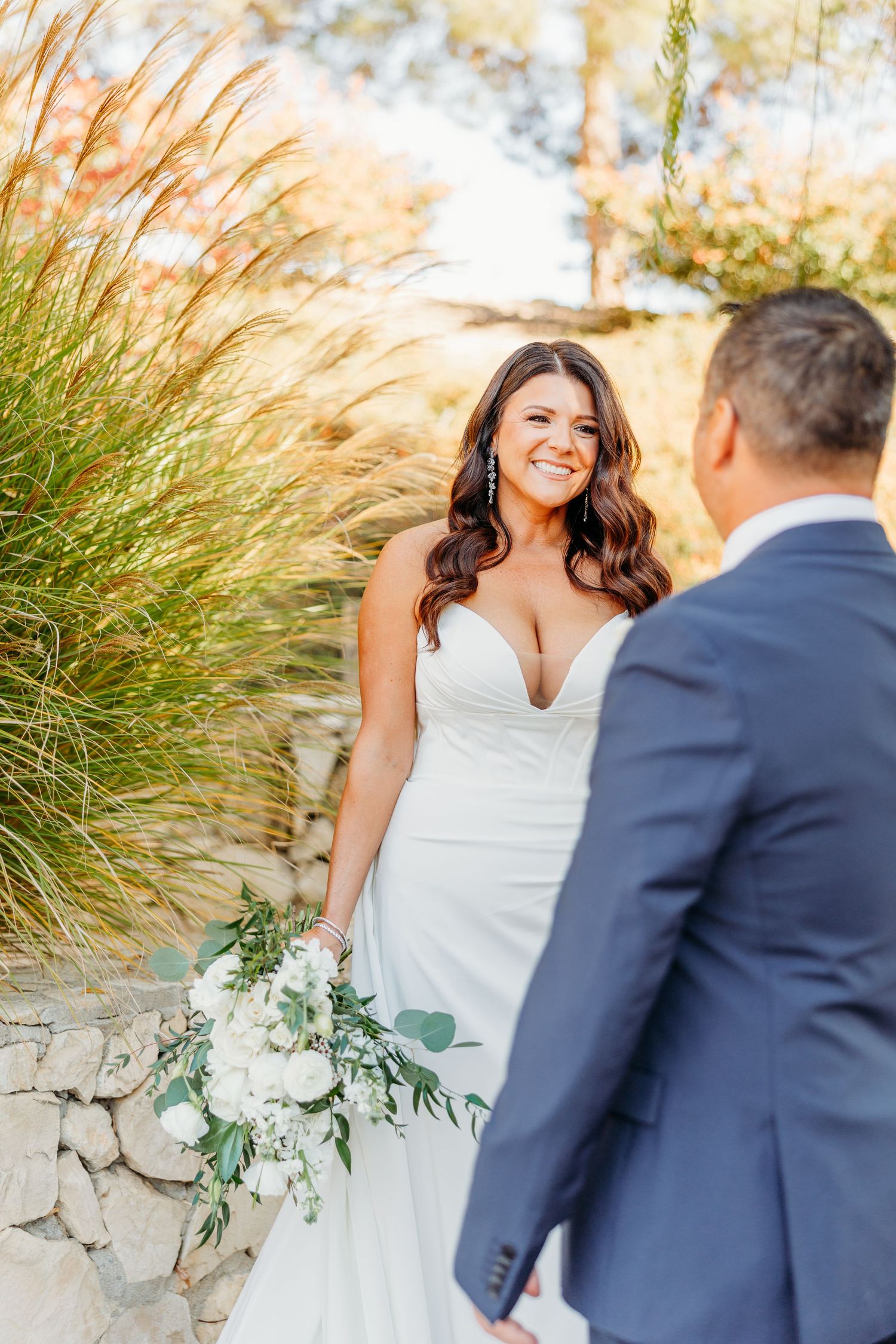 Bride in white dress and groom in navy suit share moments on stone steps surrounded by greenery.