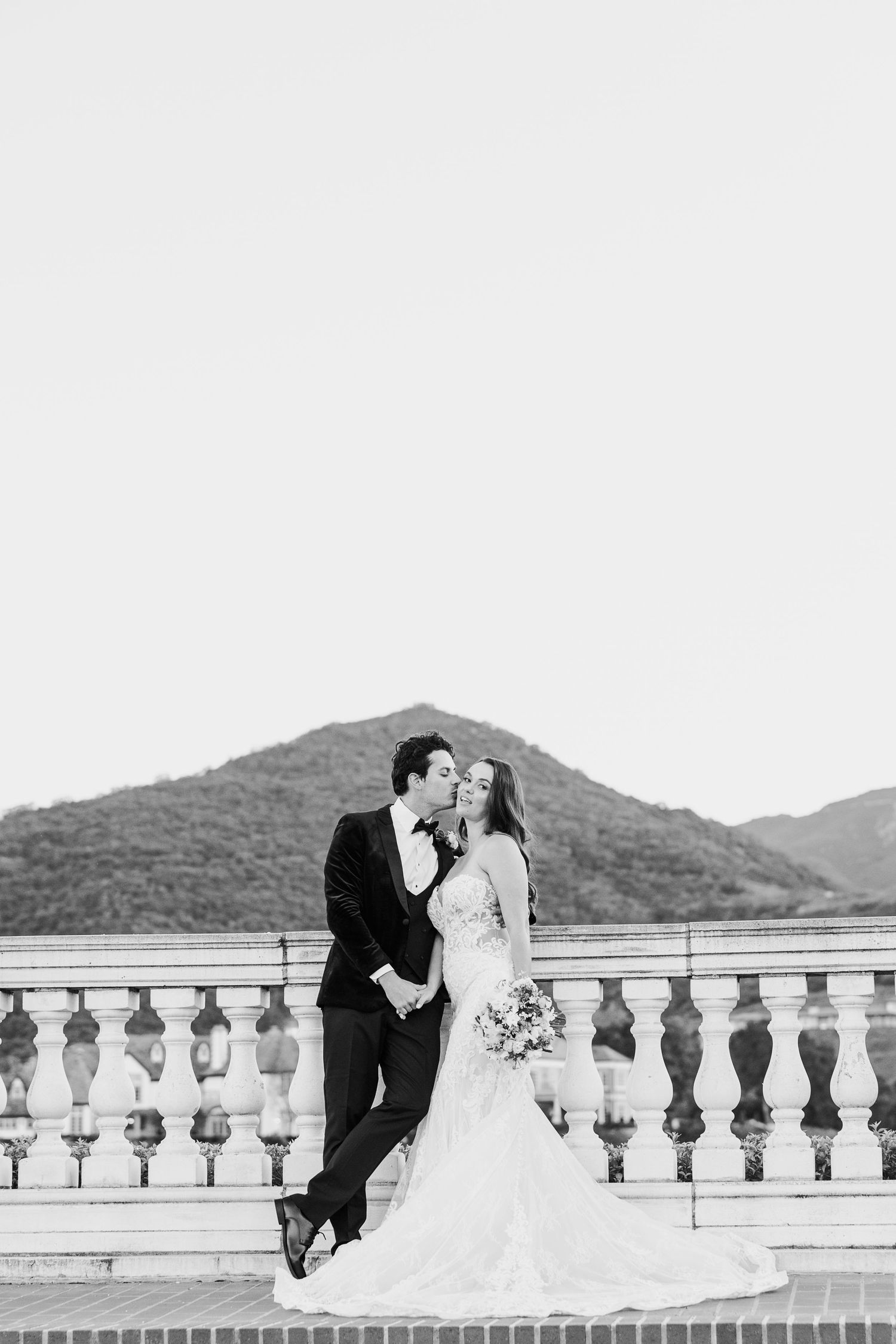 Black and white wedding photos of a couple sitting on a balcony with mountain views in the background.