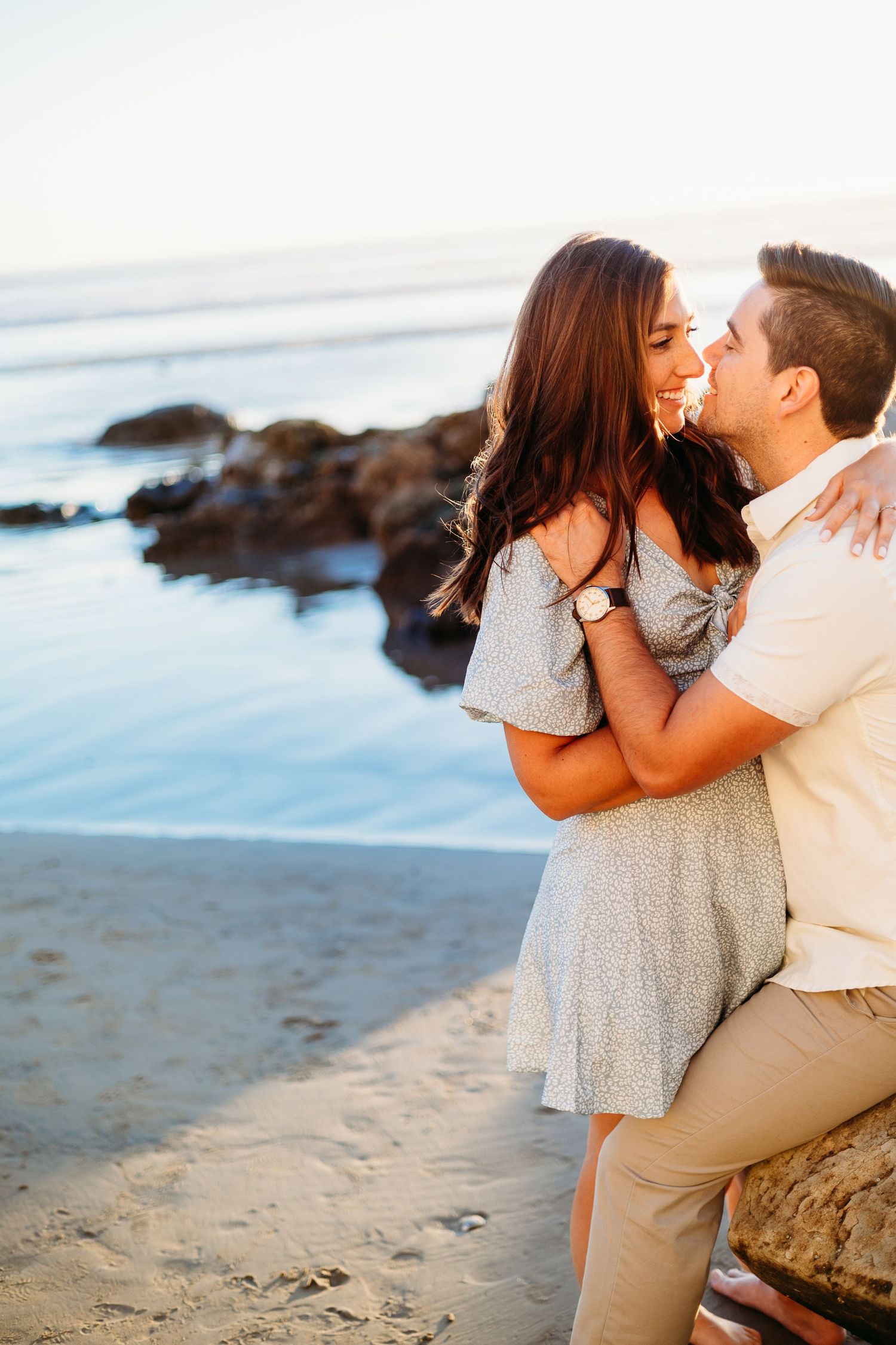 A couple shares a tender moment on rocky beach during golden hour.