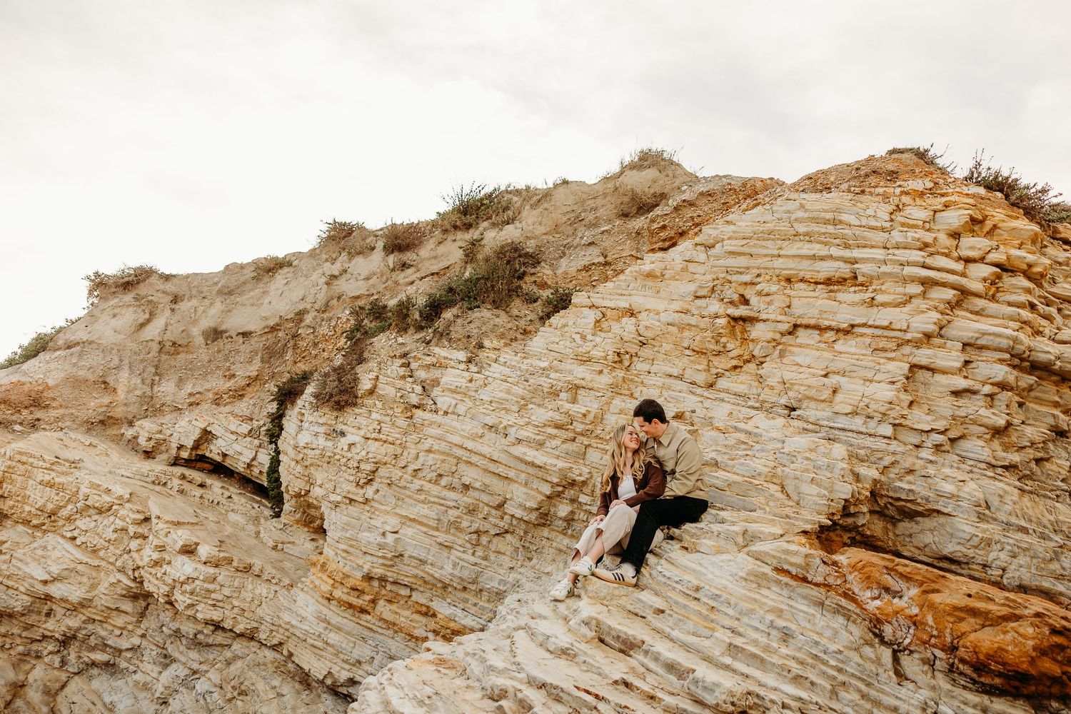 Figures stand atop rugged coastal rock formations during a sunset photoshoot.