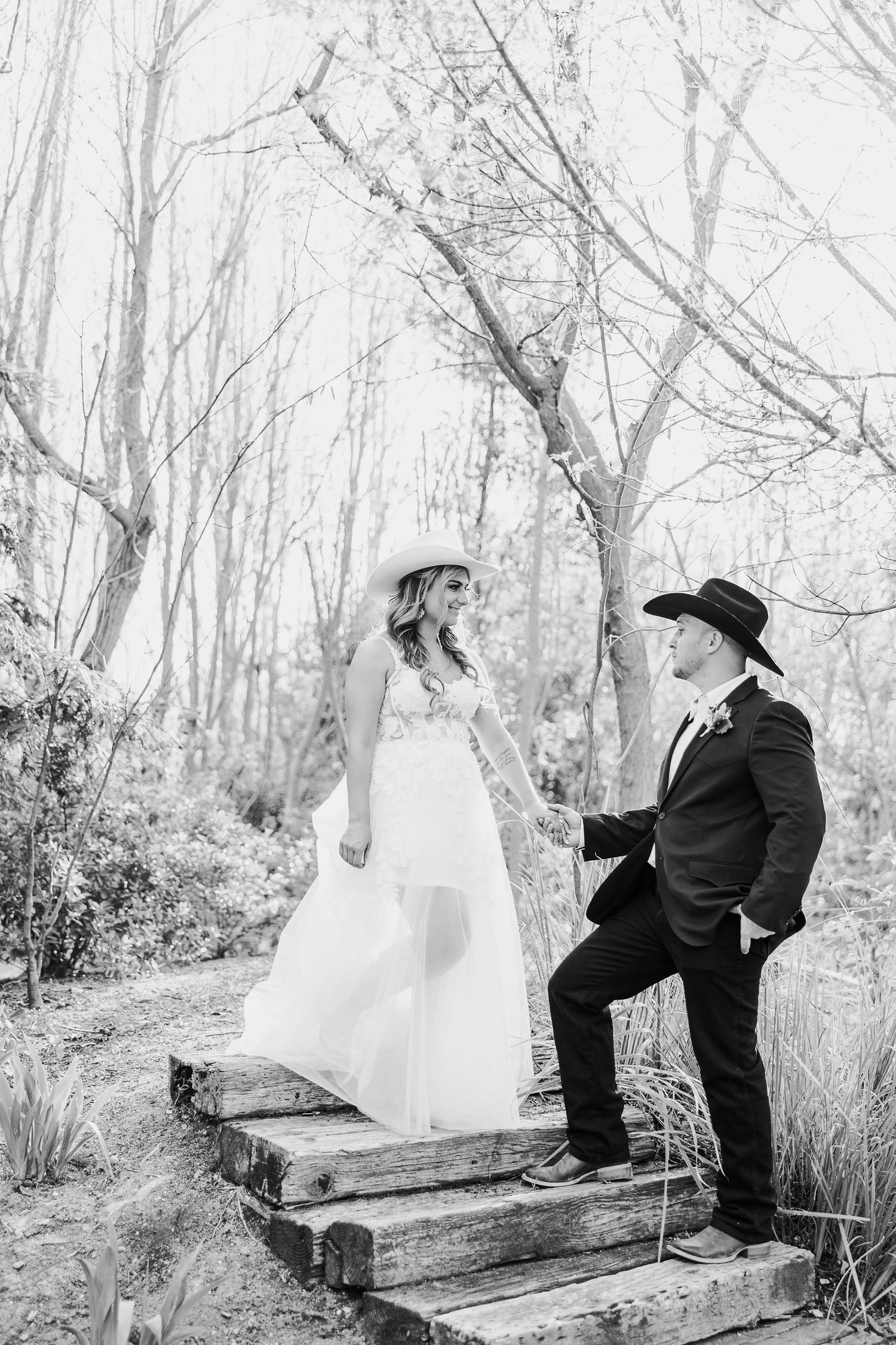 A black and white wedding photo of a couple on wooden steps surrounded by bare winter trees.