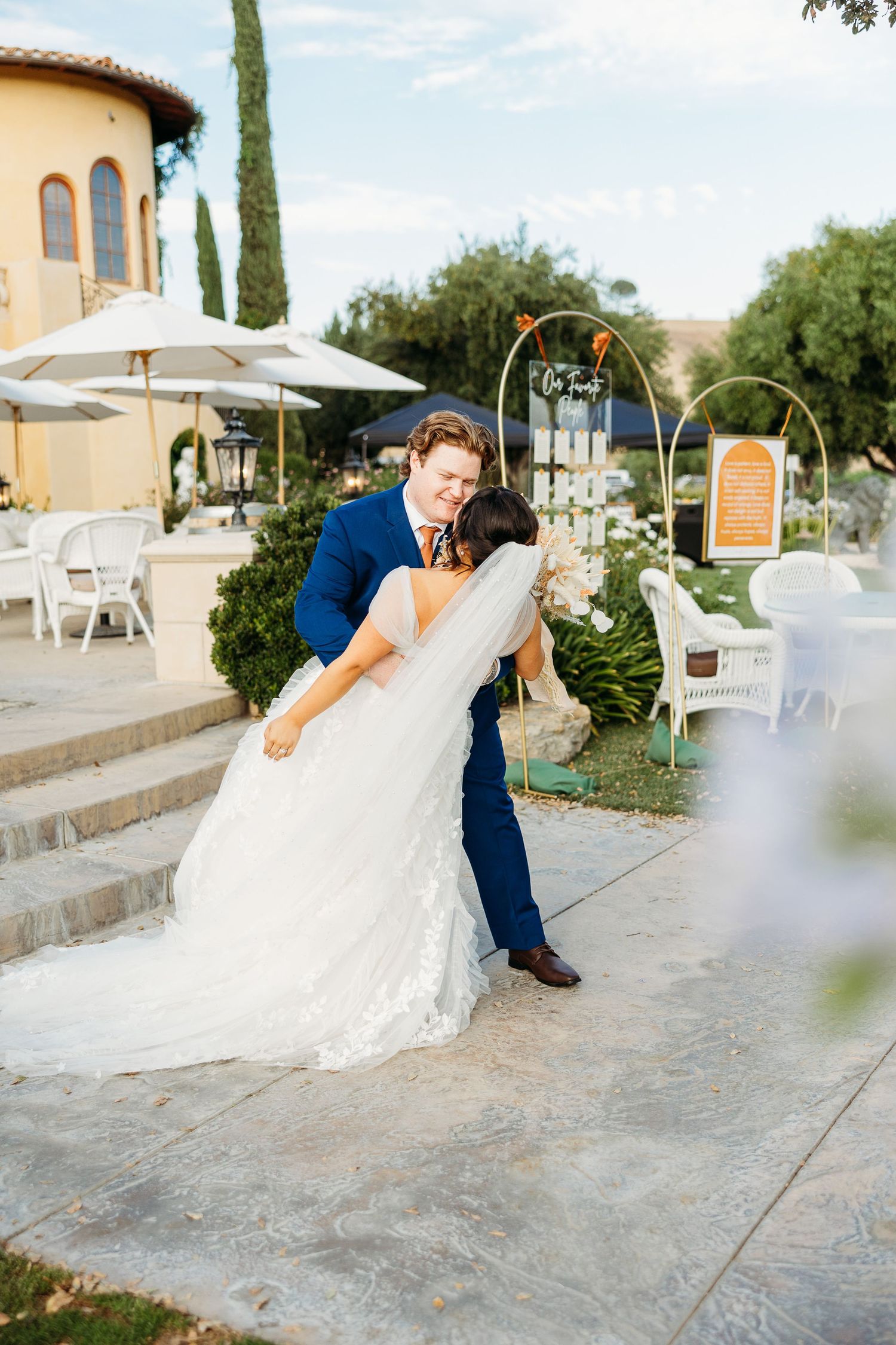 Romantic moment captured at Mediterranean villa with fountain and white umbrellas in background.