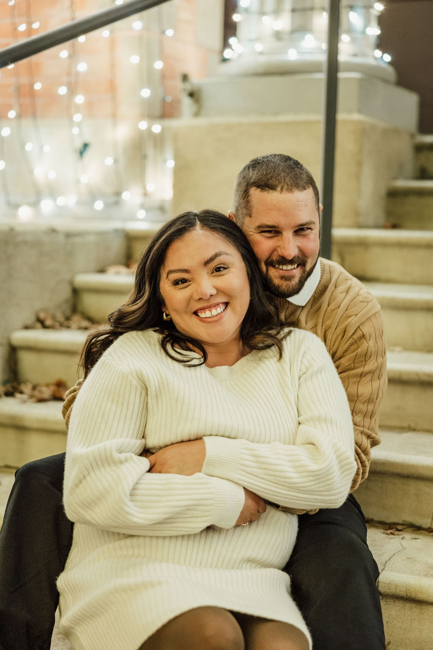 A couple shares joyful moments in a cozy indoor setting with twinkling lights in the background.