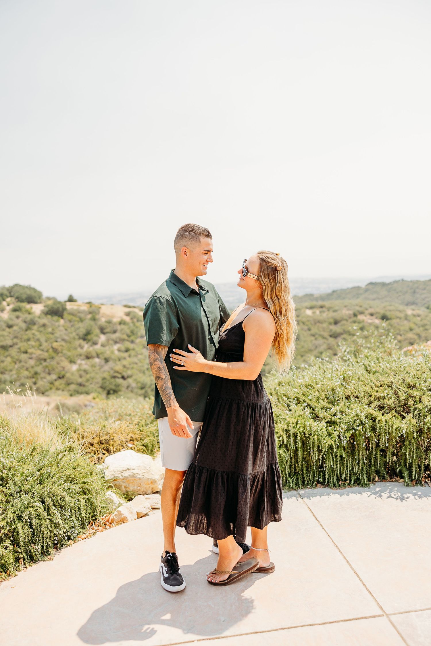 A couple shares intimate moments during a sunset photoshoot on an outdoor patio with scenic views.