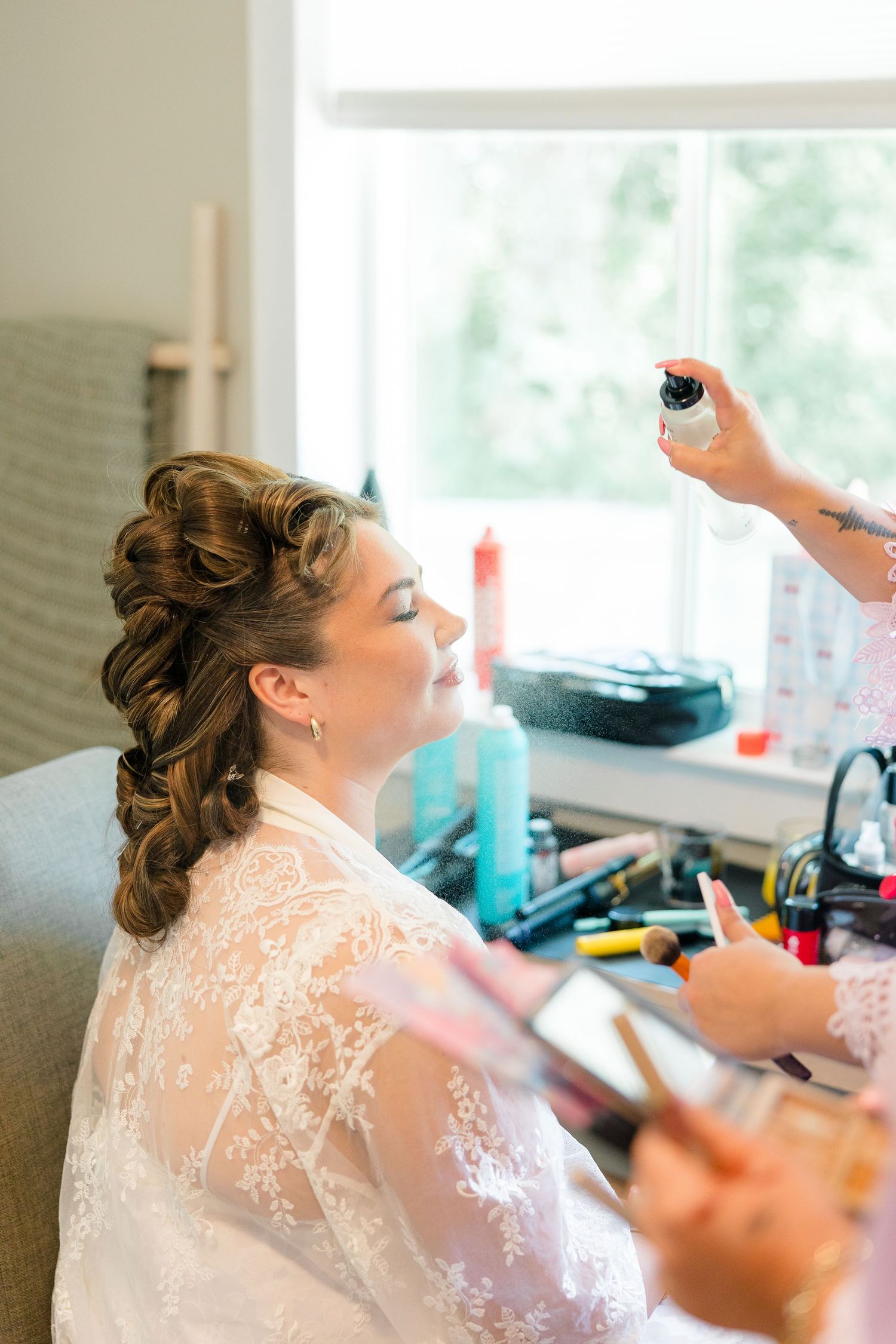Bride getting makeup set with hairspray by a stylist before her wedding day.