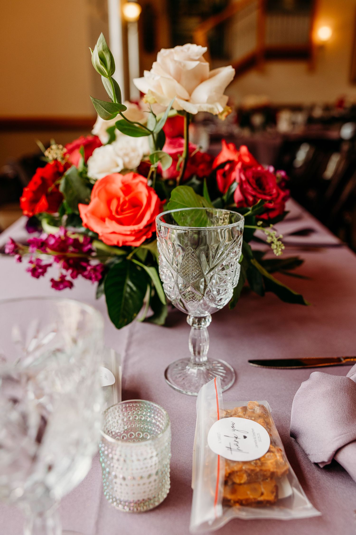 Elegant table setting with crystal glassware and pink and red floral centerpieces at a formal event.