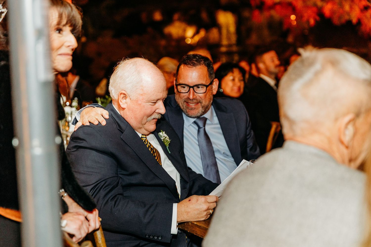 Guests mingling at an evening outdoor wedding reception with warm lighting and fall decorations.