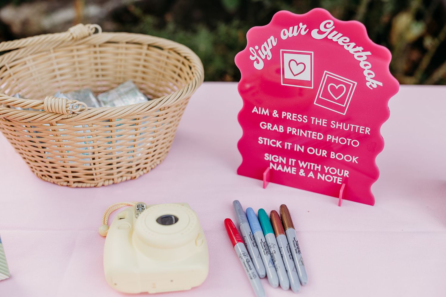 Pink social media photo booth signs displayed with wicker baskets and colorful markers.