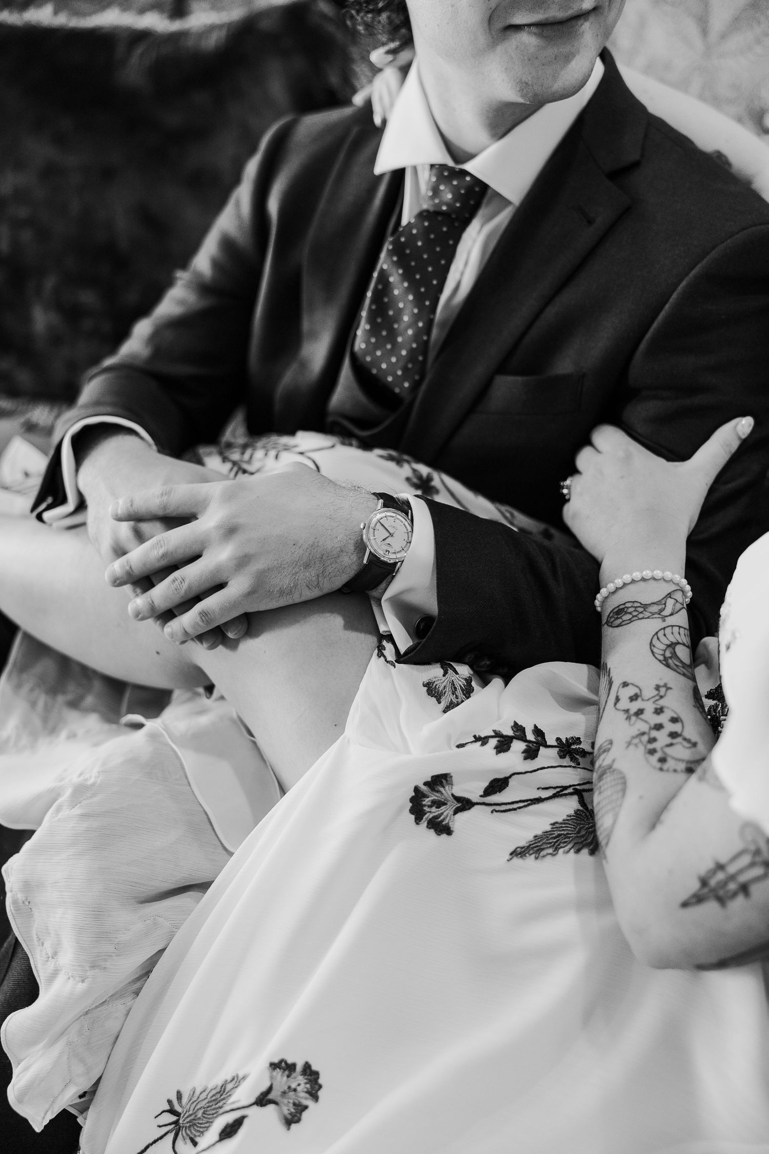 Black and white detail shot of tattooed arms and formal attire.