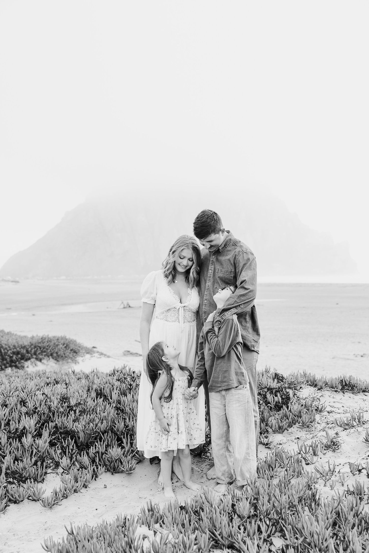 A couple shares intimate moments along a coastal path with mountains in the background.