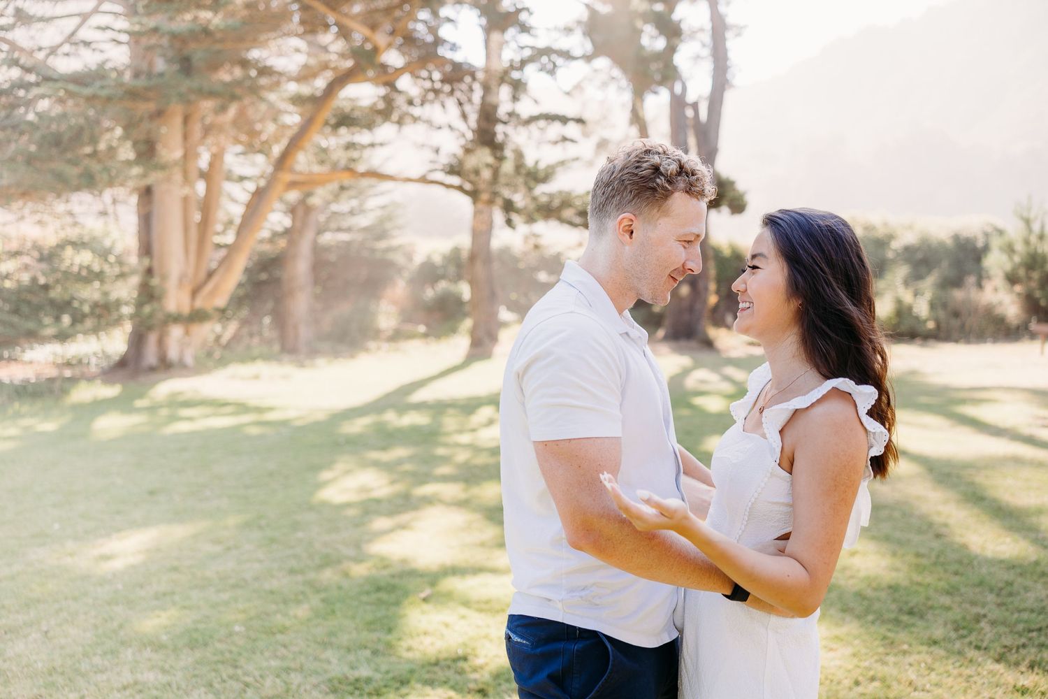 Romantic couple embracing outdoors in a sunny garden setting with trees in the background.