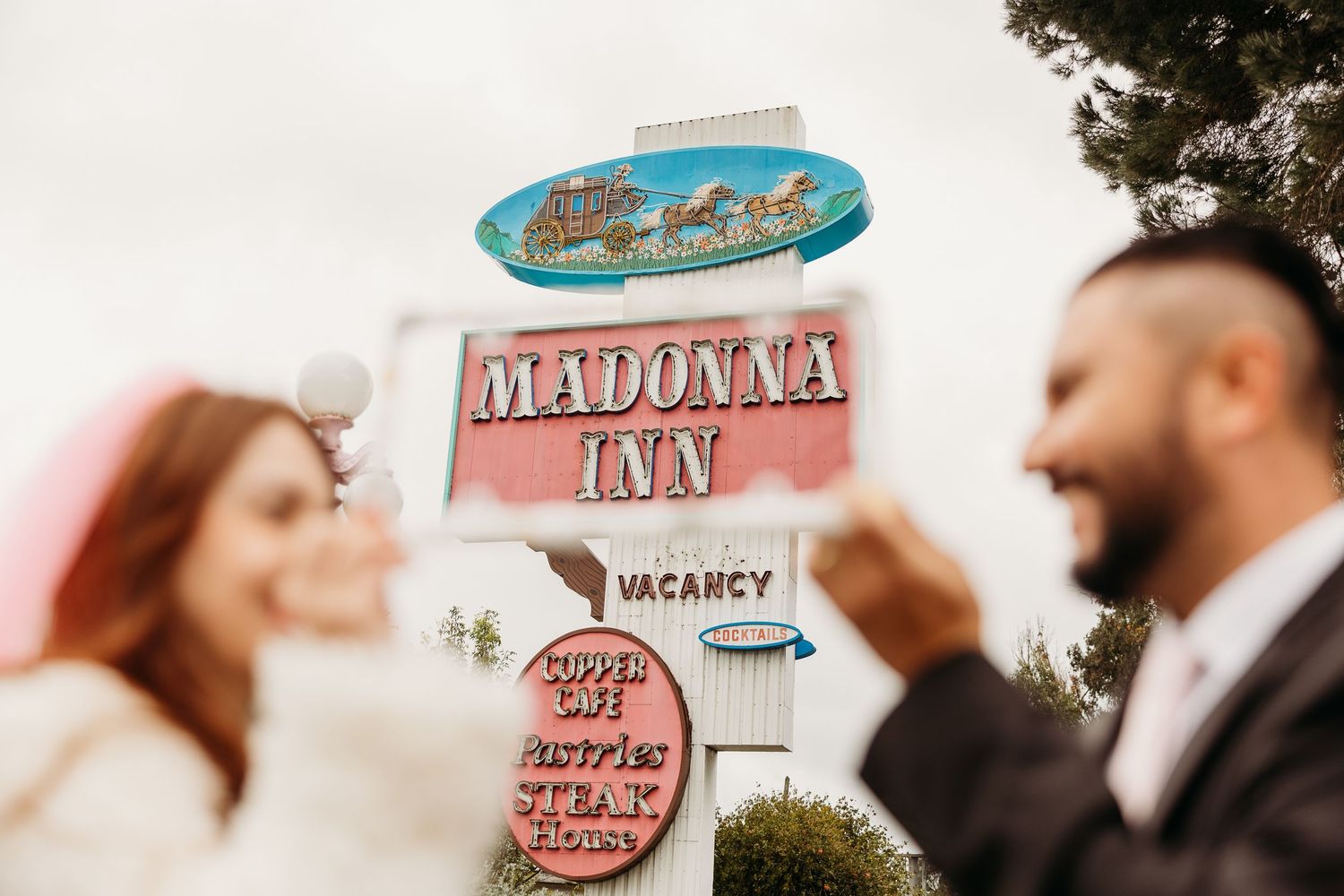 Blurred couple stands in front of vintage Madonna Inn motel sign with blue oval logo in San Luis Obispo.