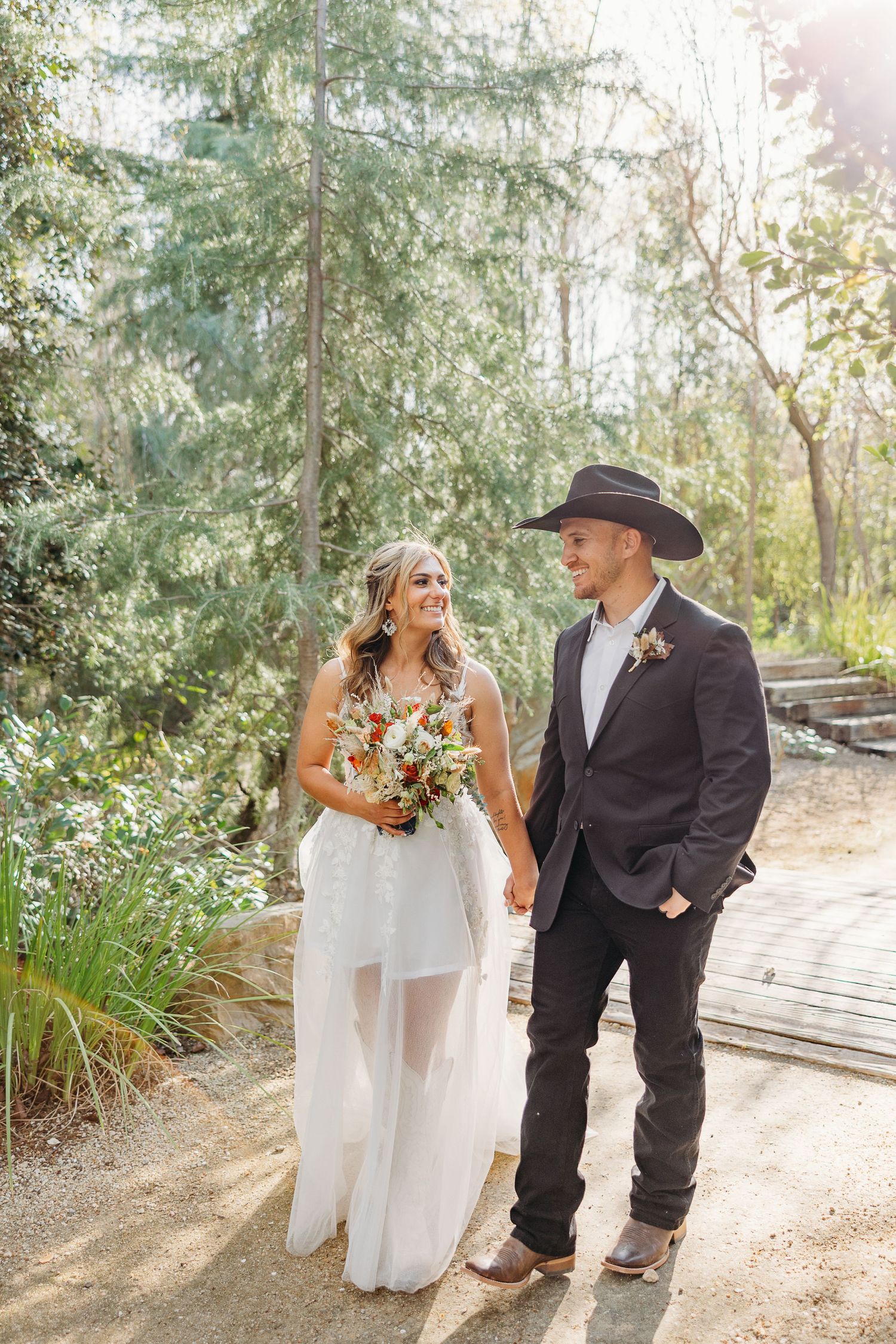 A couple sharing a joyful moment on a sunlit garden path with natural greenery and flowers.