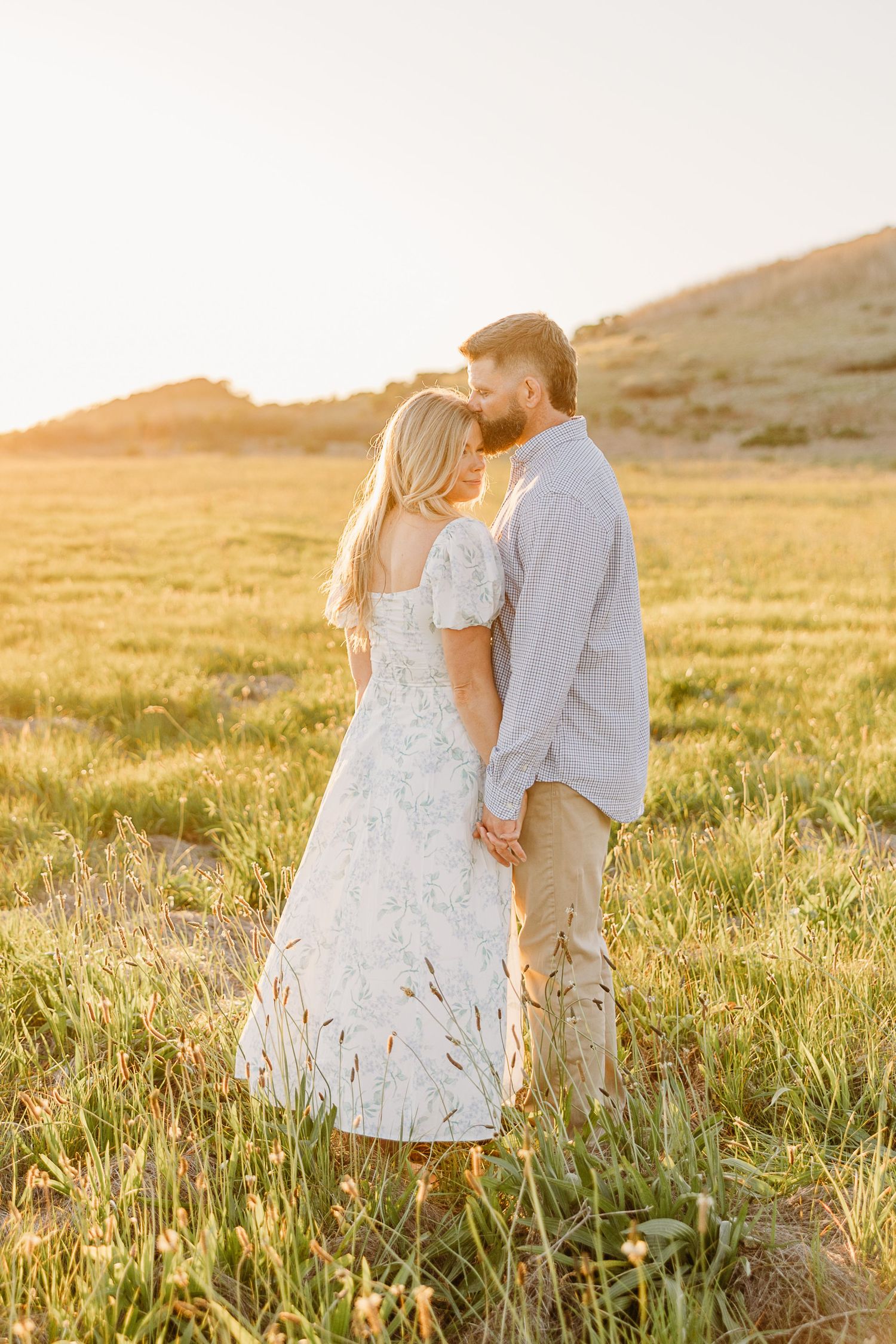 Romantic couple embraces in a sunlit meadow at golden hour wearing casual summer attire.