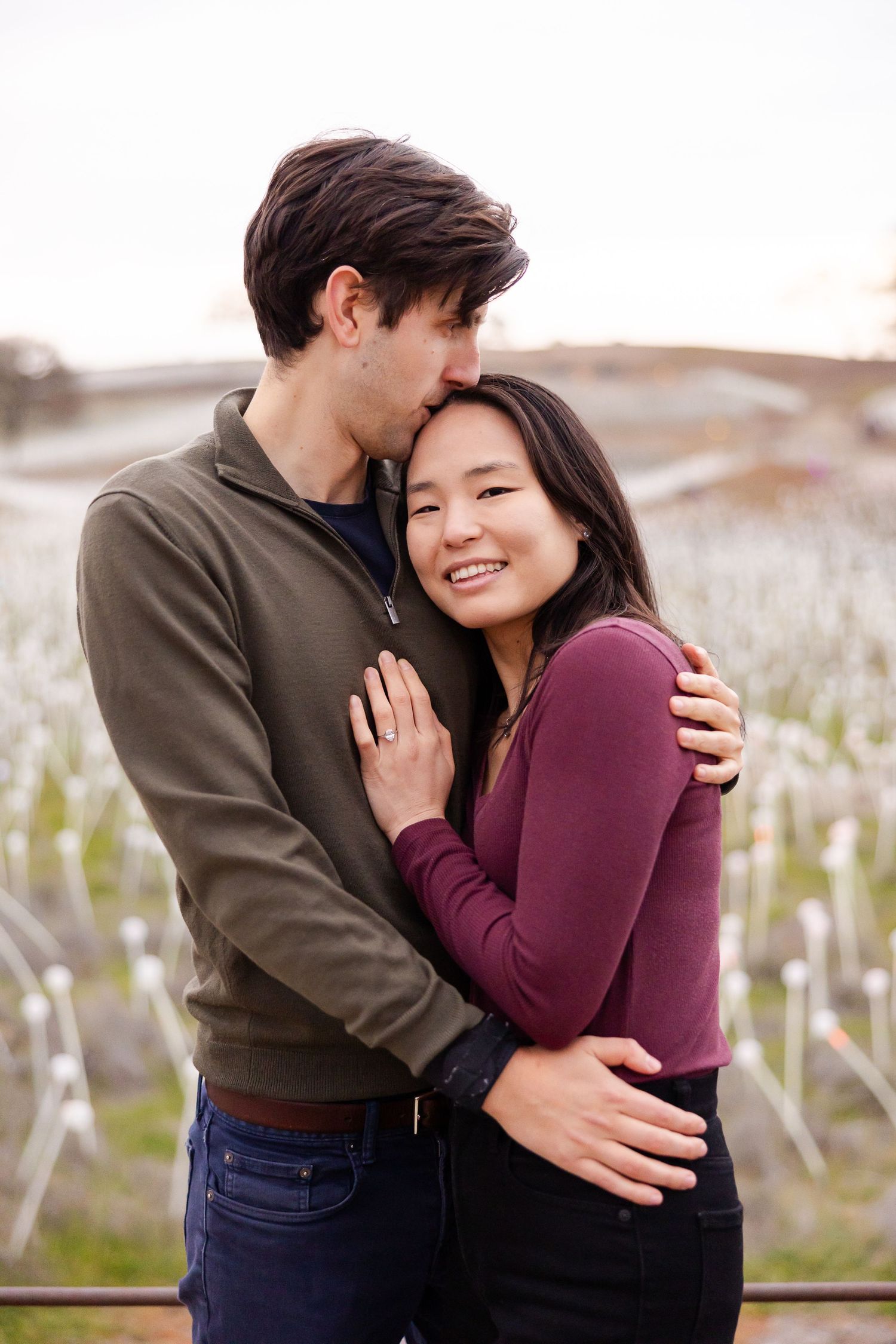 A couple laughs and embraces while standing in a rustic outdoor setting.