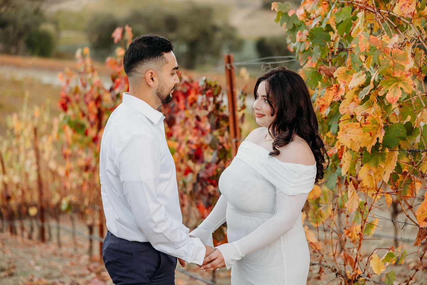 A couple shares a romantic moment in a vineyard with fall-colored leaves in the background.