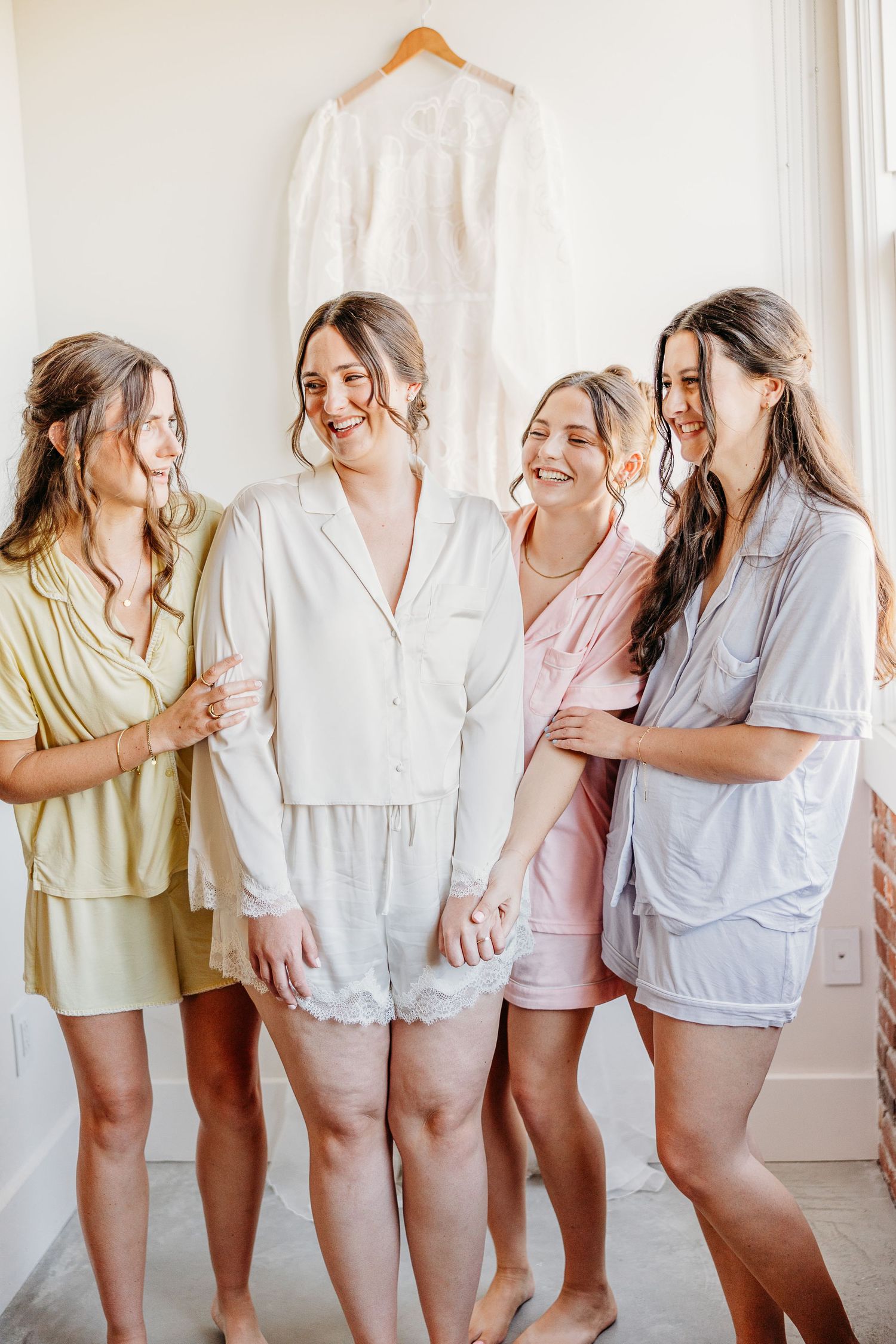 Bridesmaids in pastel sleepwear share laughter during wedding preparations.