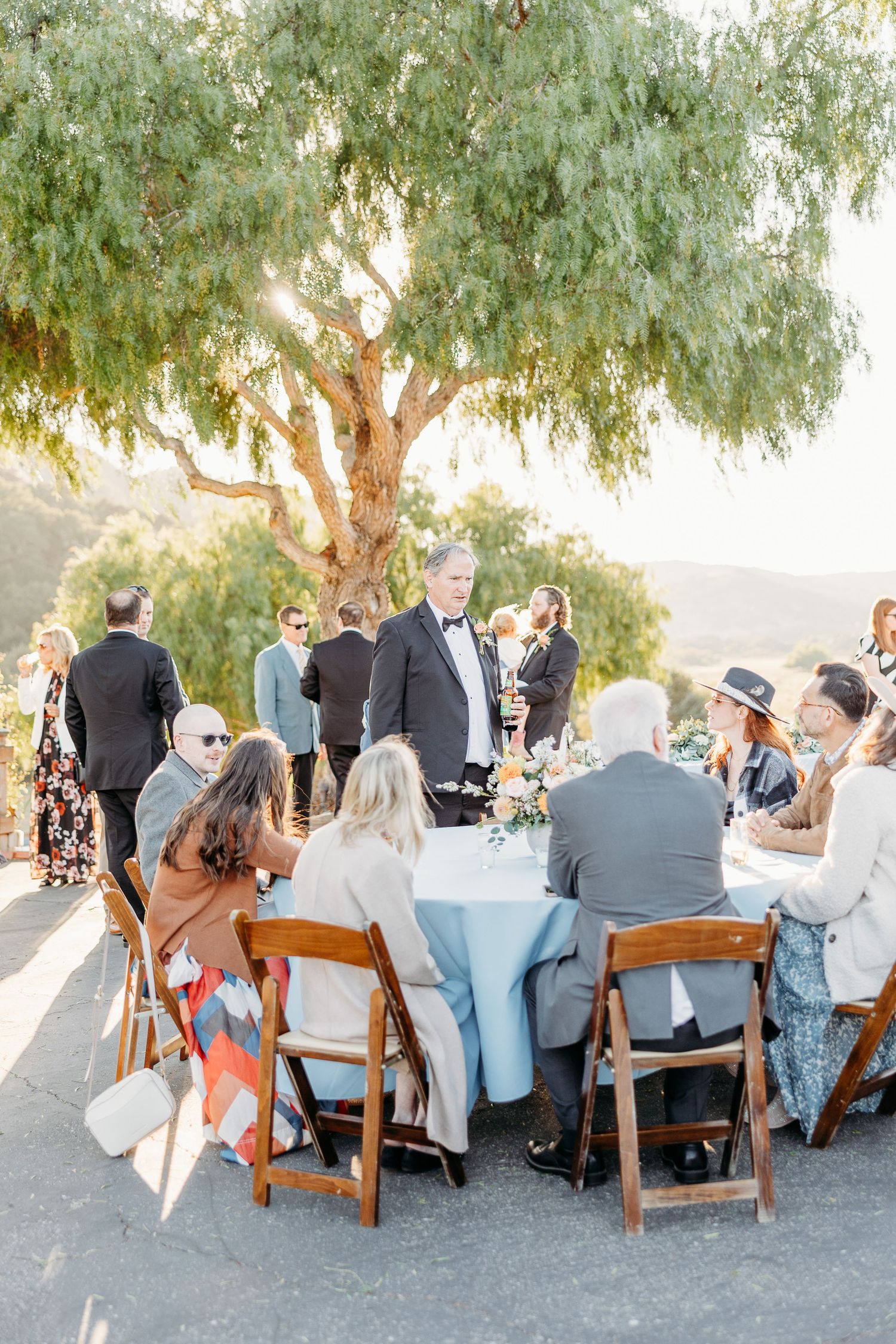 Outdoor reception dining setup under eucalyptus trees during golden hour.