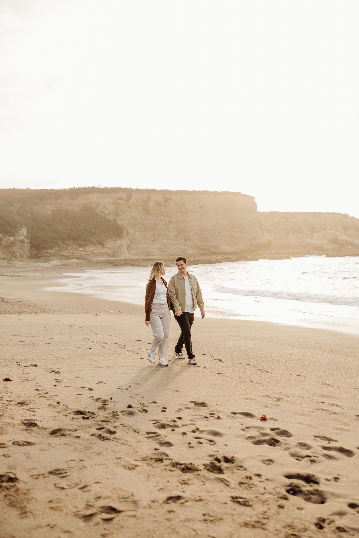 A couple strolls along a serene beach on an overcast day in sepia tones.