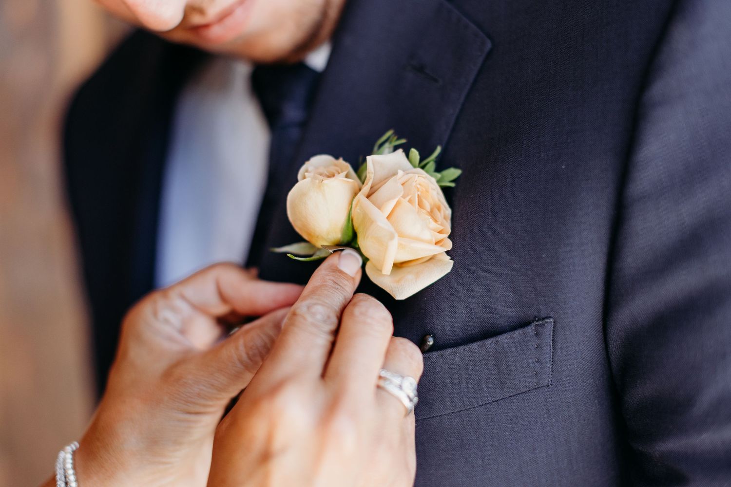 Close-up of peach rose boutonnieres pinned to dark navy suit jackets.