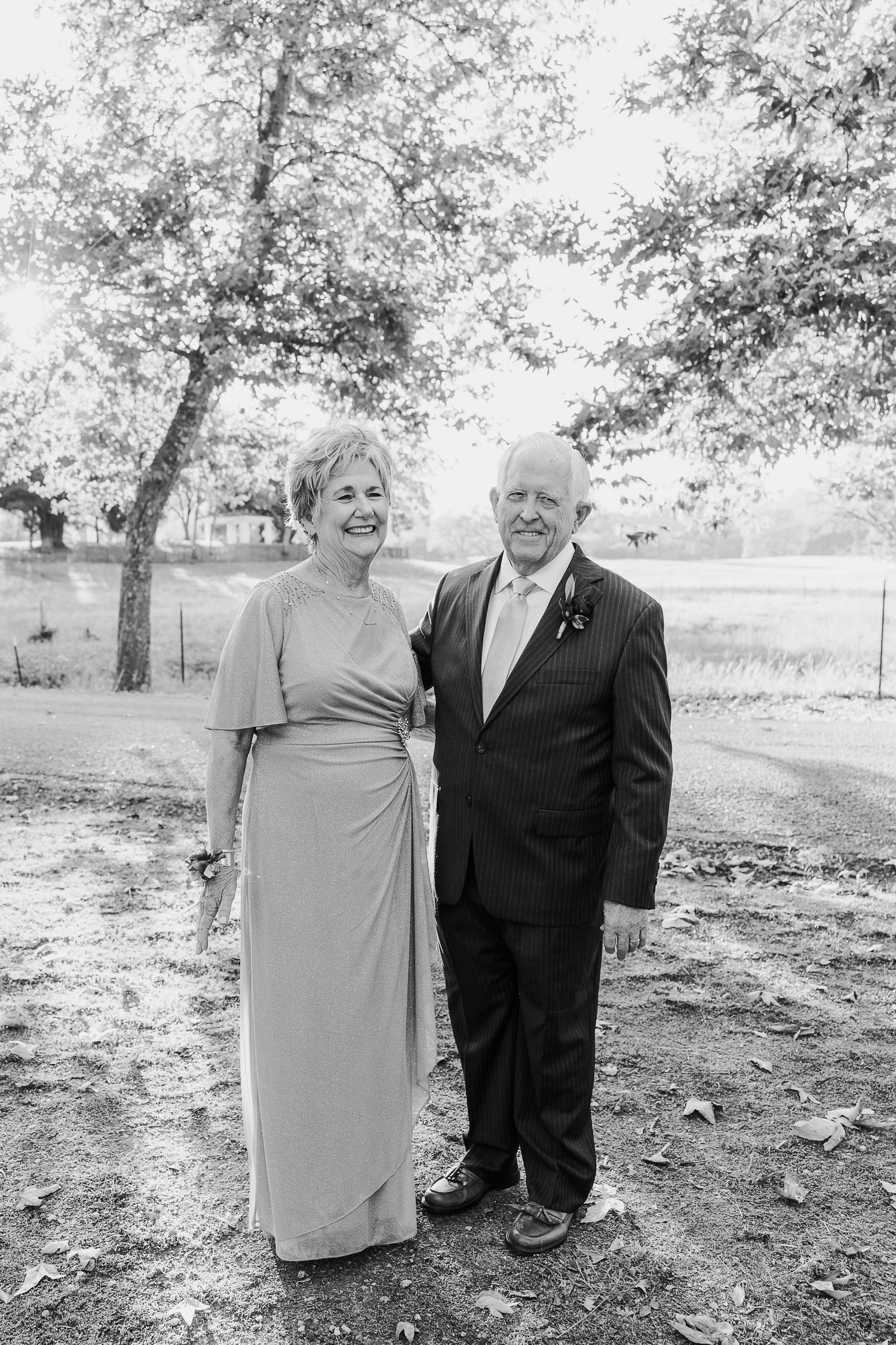 Black and white outdoor portrait of a couple standing together under autumn trees.