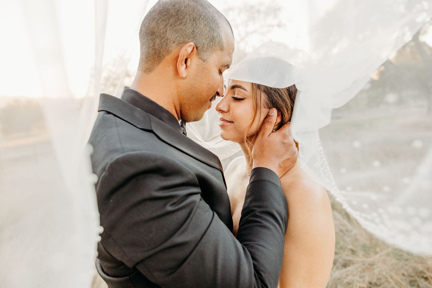 An intimate wedding portrait of a couple sharing a tender moment against a bright background.