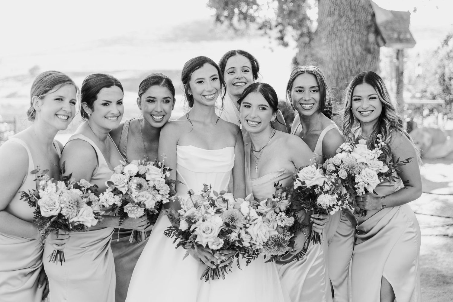 Wedding party members in pale blue bridesmaid dresses pose together with bouquets outdoors.
