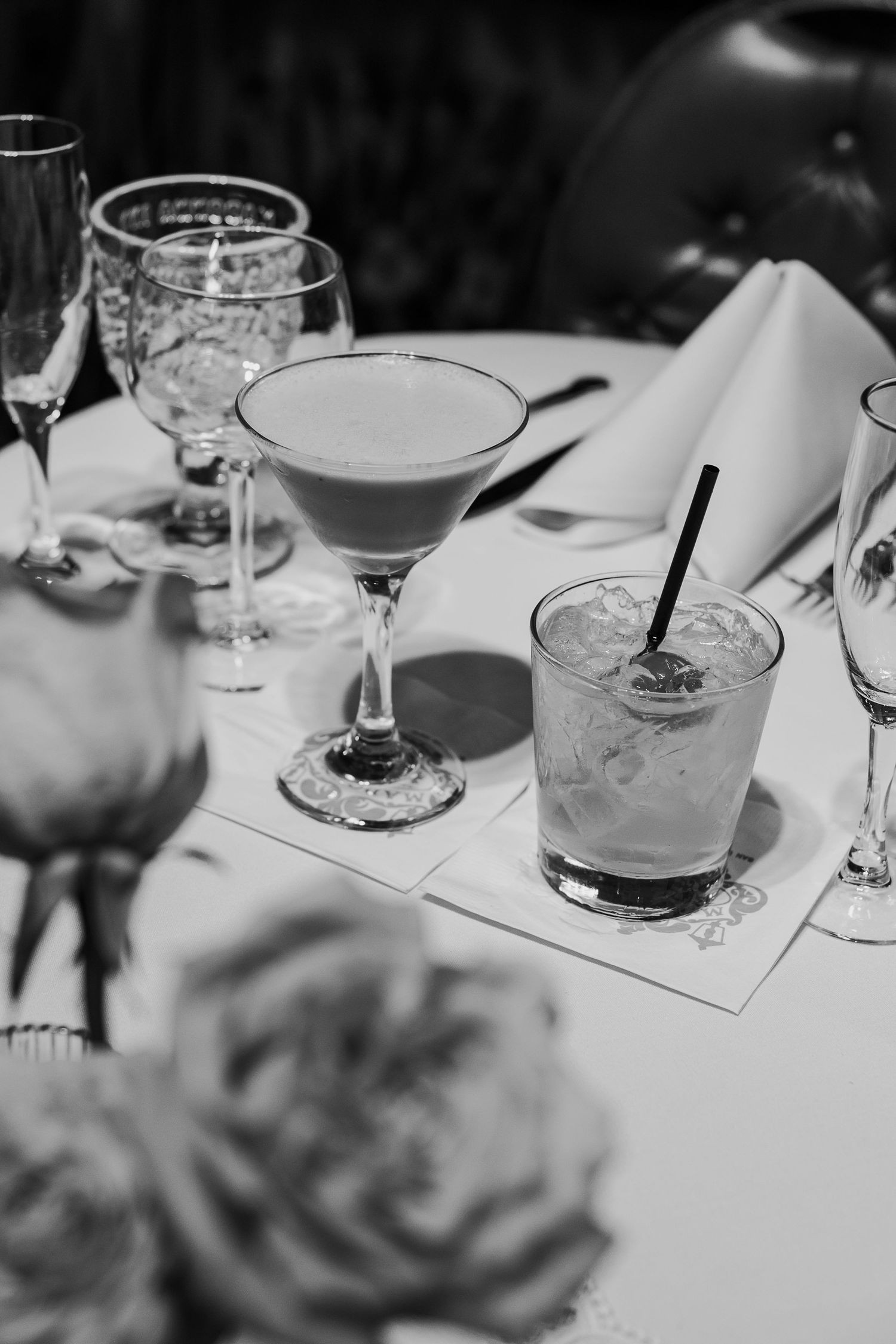 Black and white photograph of elegant cocktails and wine glasses arranged on a table at an upscale event.