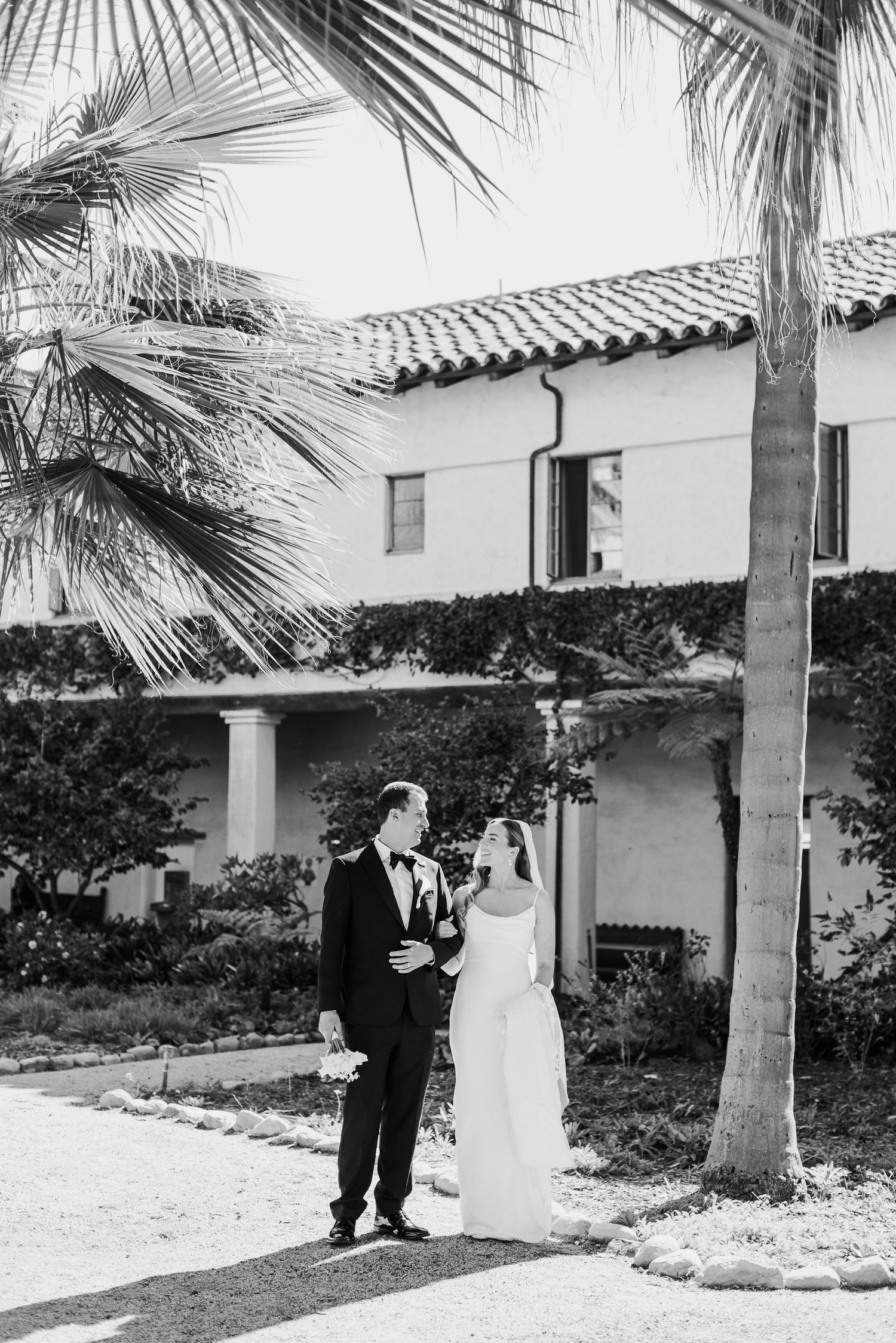 A series of black and white wedding photos showing a couple walking through an elegant Spanish-style courtyard.