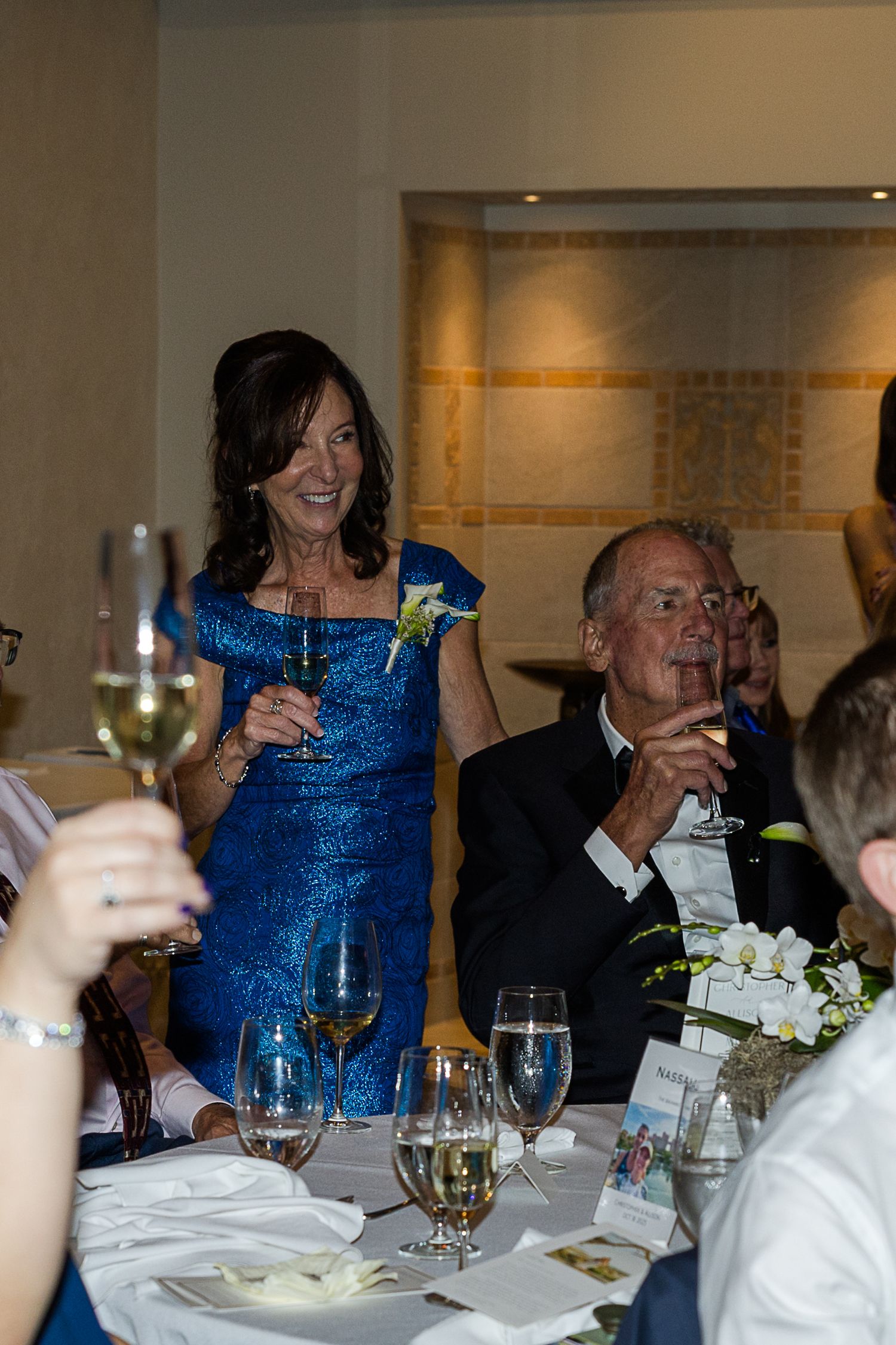 Wedding reception dinner scene with guests raising glasses for a toast at an elegant indoor venue.