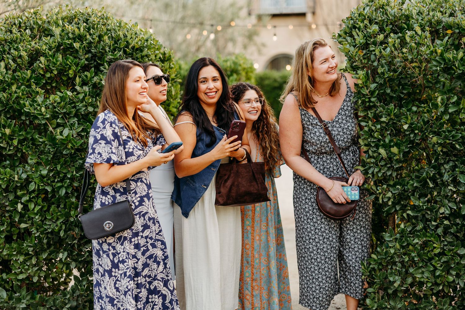 Group of friends in summer dresses laughing together in a garden setting.