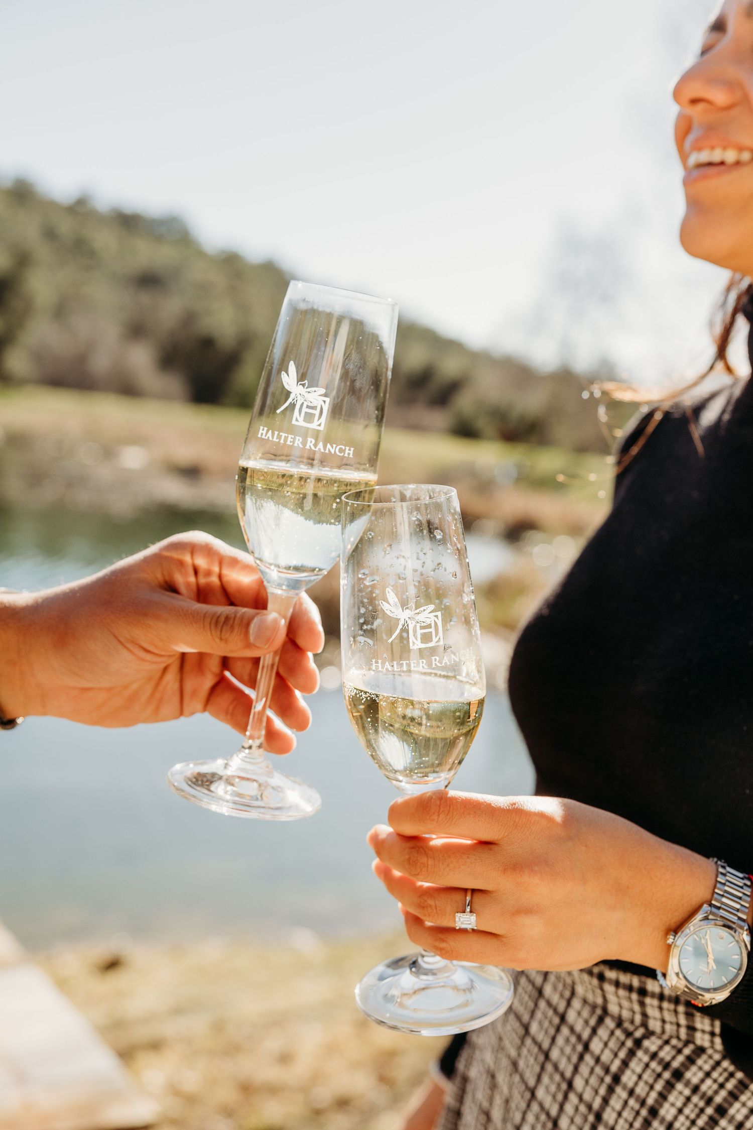 Close-up shots of hands holding wine glasses with etched designs against a waterfront background.