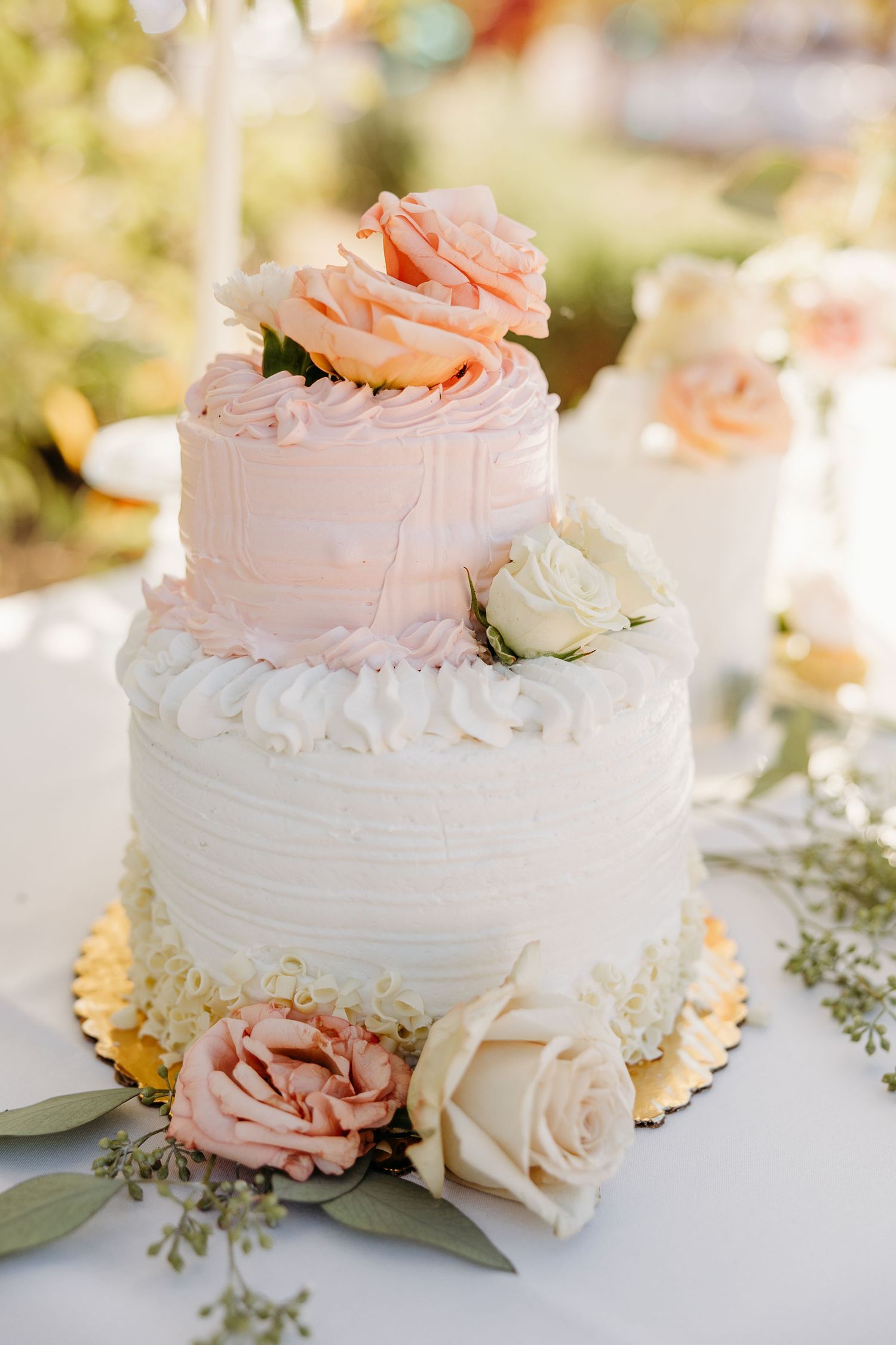 White wedding cakes decorated with delicate pink roses and floral accents on a reception table.