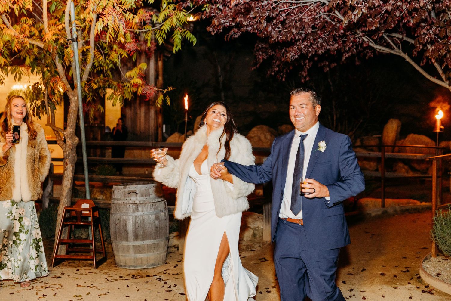 Wedding celebration at dusk with string lights illuminating an outdoor venue and autumn foliage.