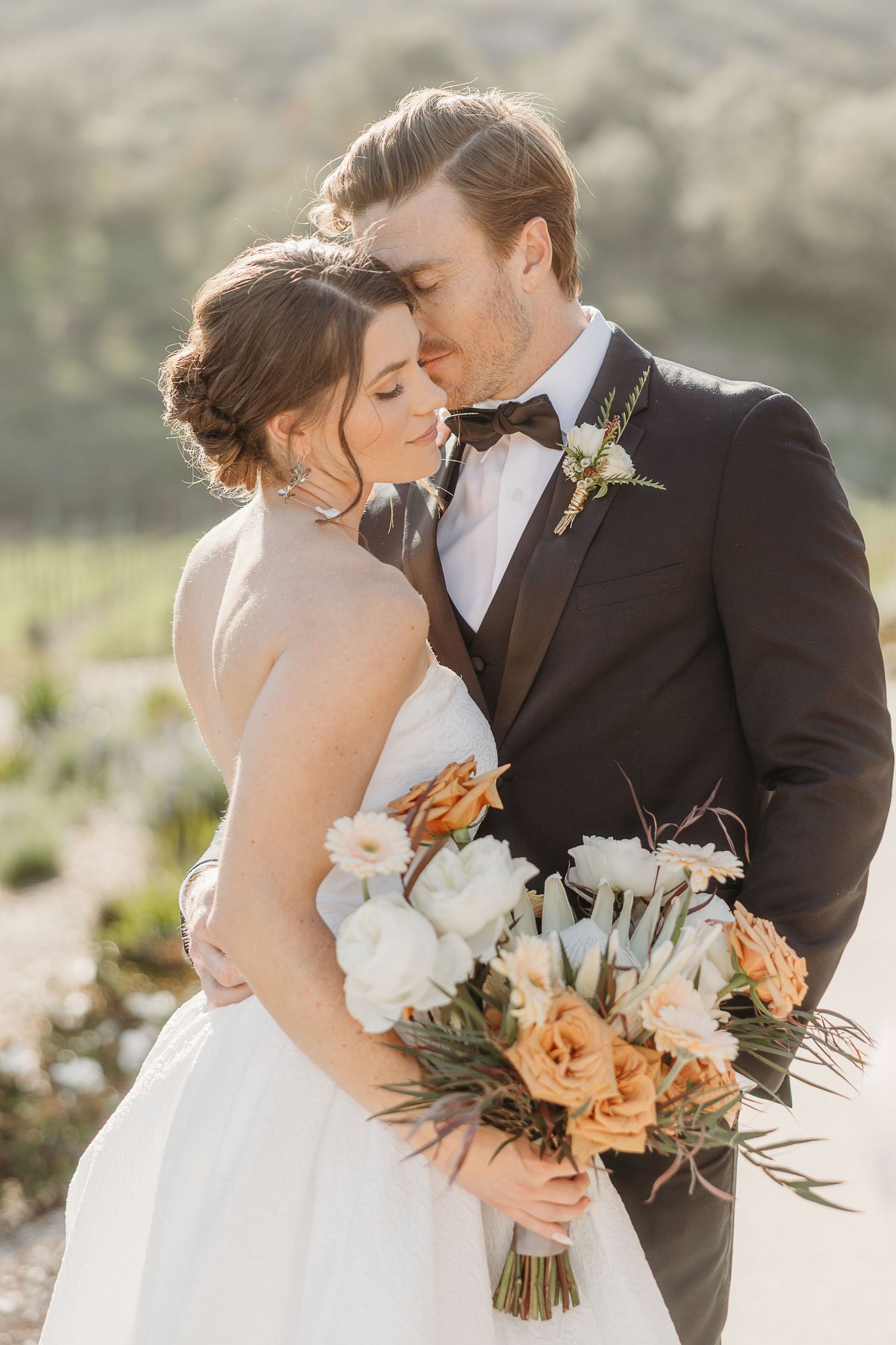 Romantic wedding portraits with couple embracing and holding peach and white floral bouquet.