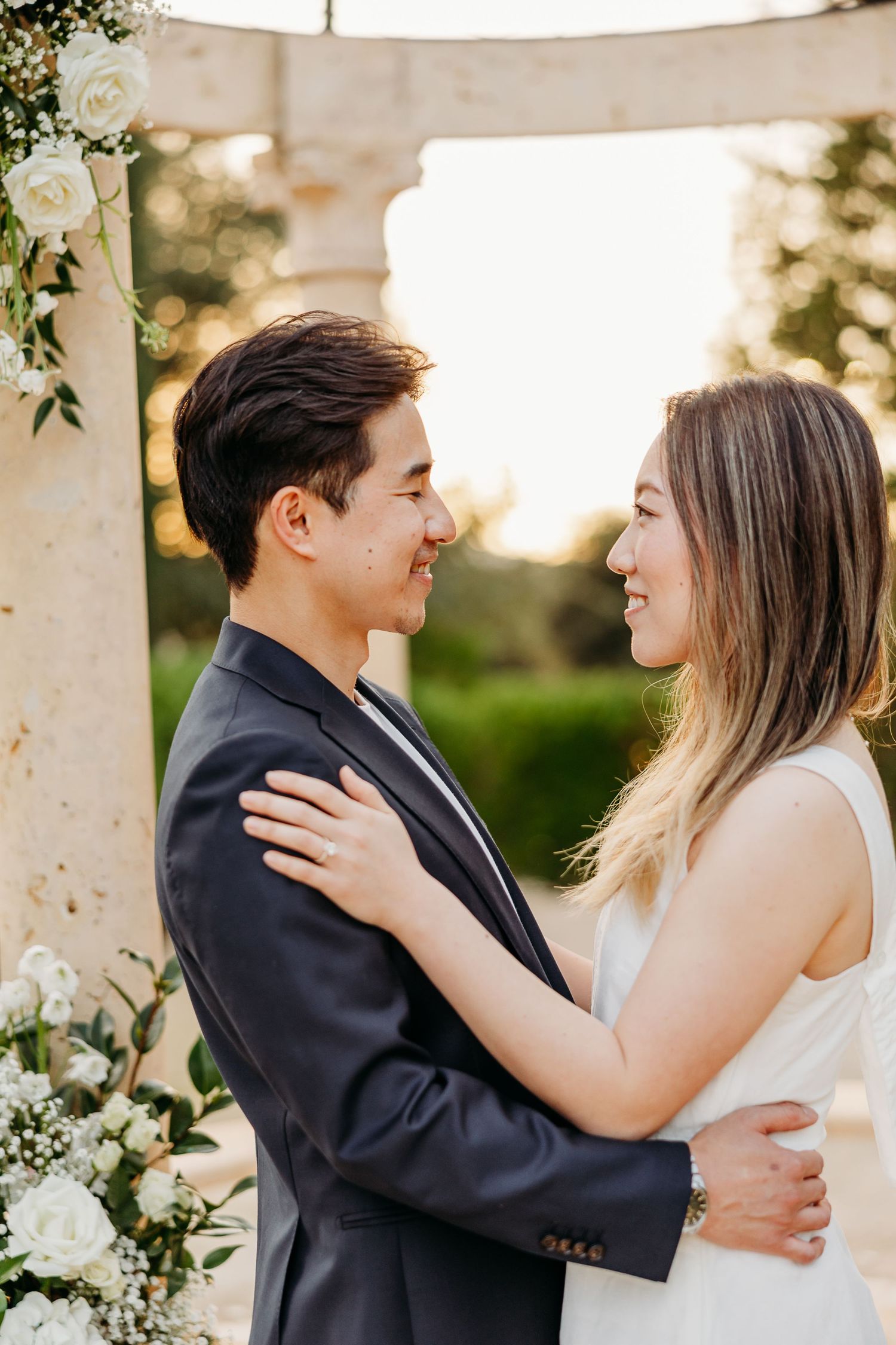 Couple embracing tenderly in an elegant outdoor setting with white floral decorations.