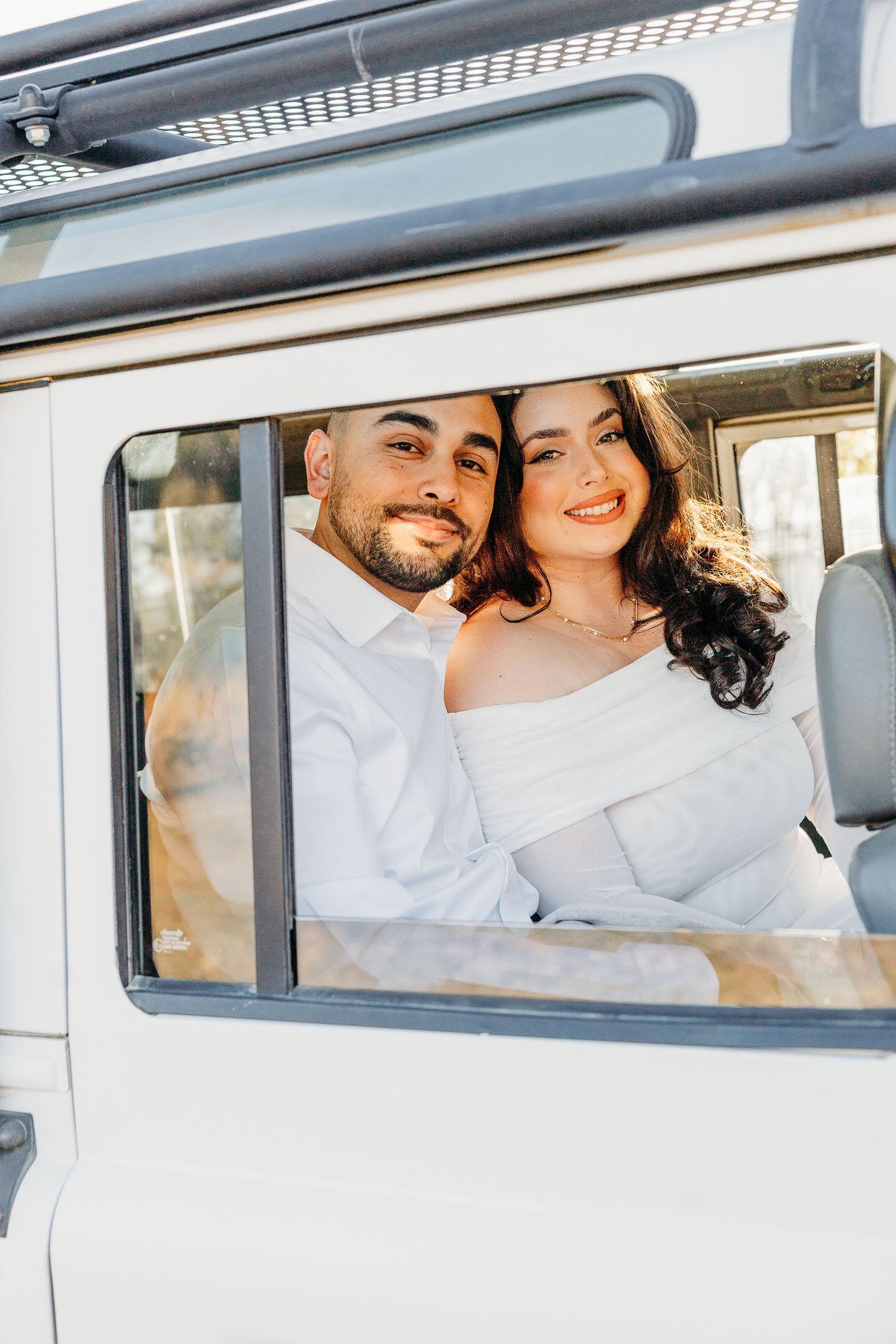 A happy couple smiles together while sitting in a vintage white van window during a sunny day.
