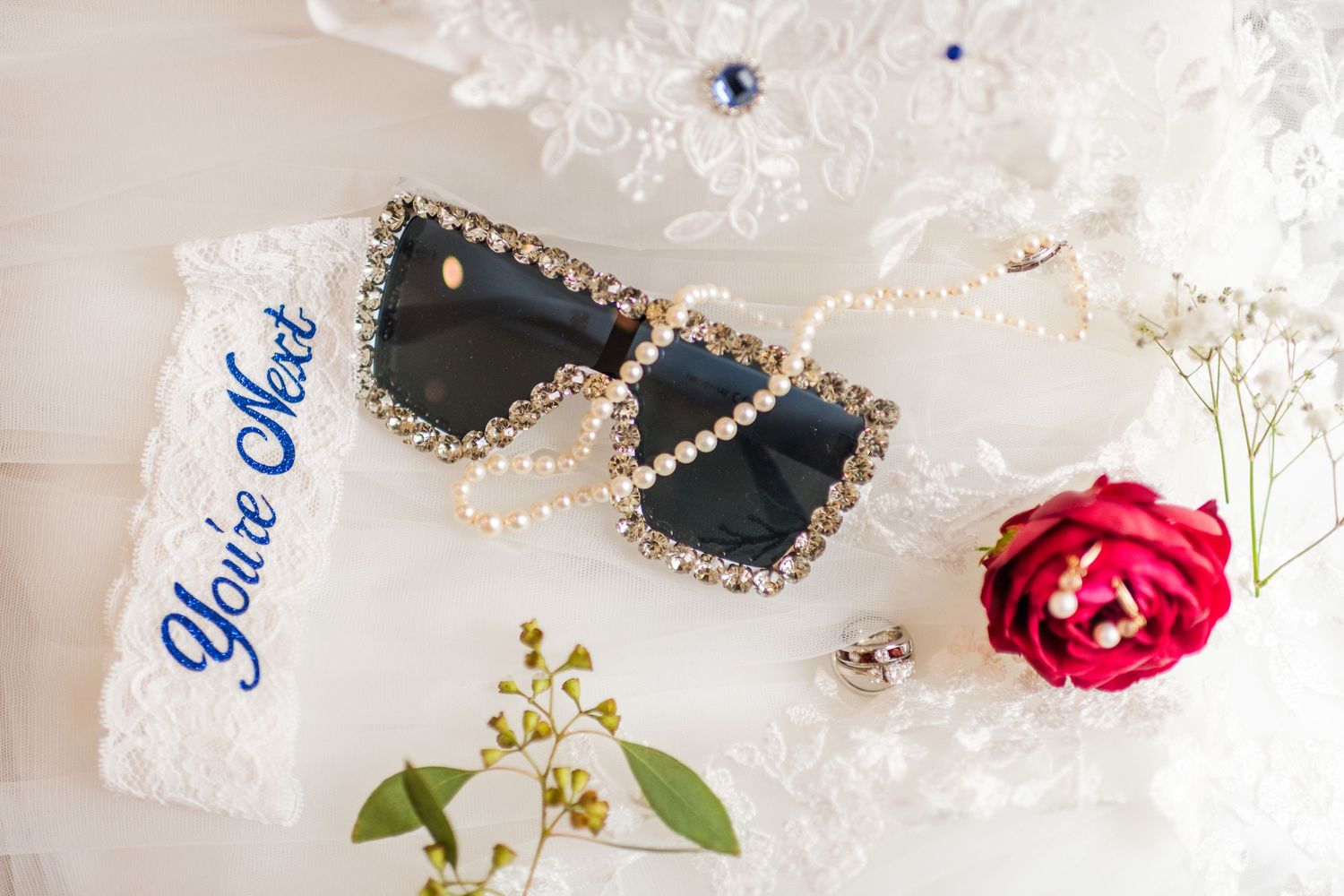 Wedding accessories including decorated sunglasses, a red rose, and delicate lace details.