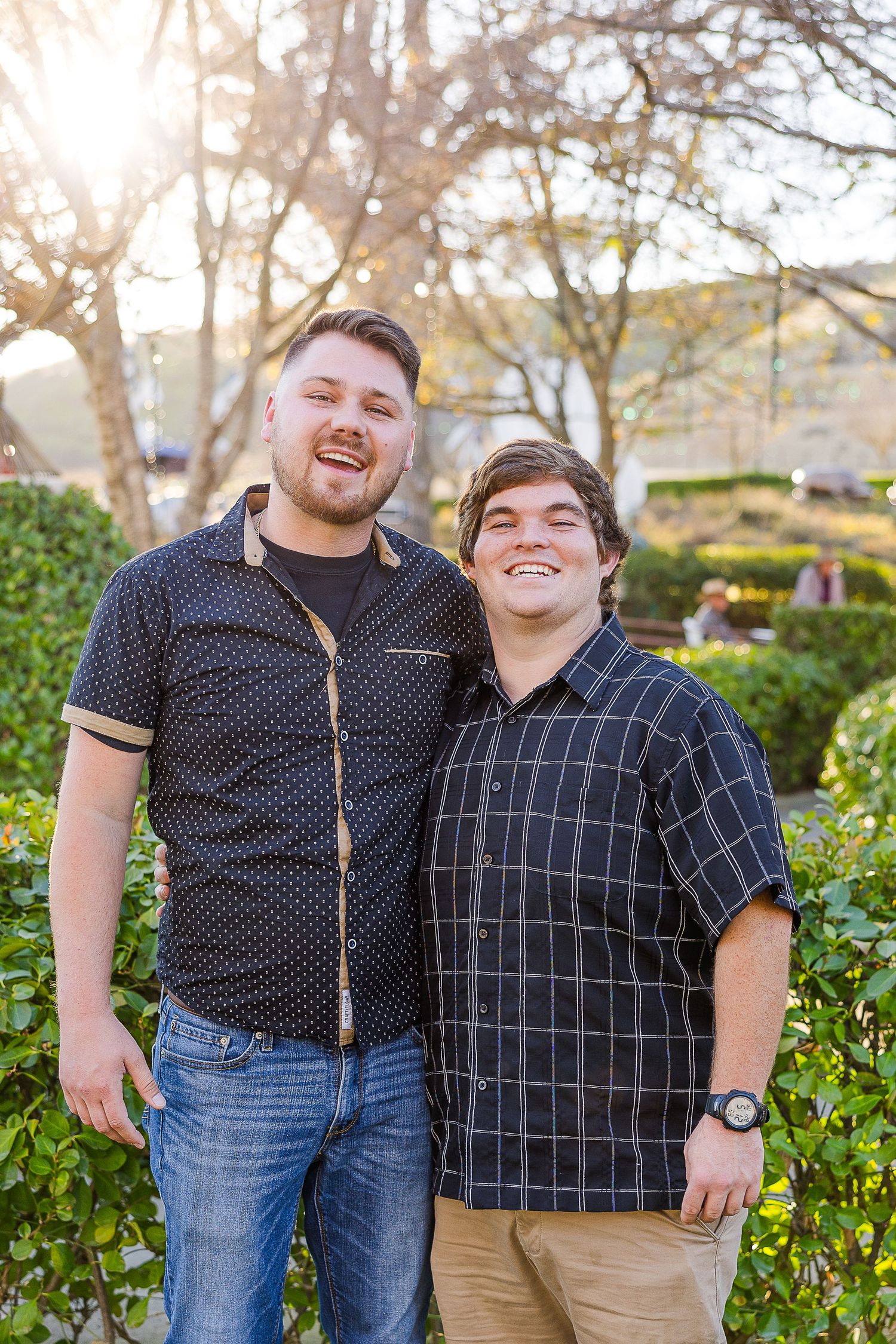 Cheerful outdoor portrait in front of sunlit garden foliage.
