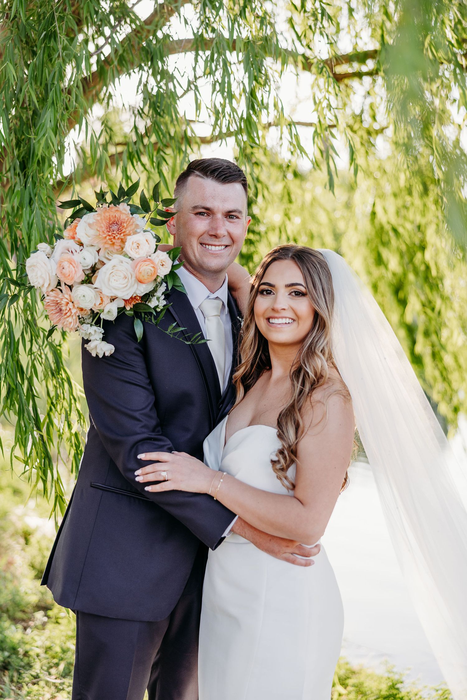 Romantic wedding portraits under weeping willow trees with peach floral bouquet.
