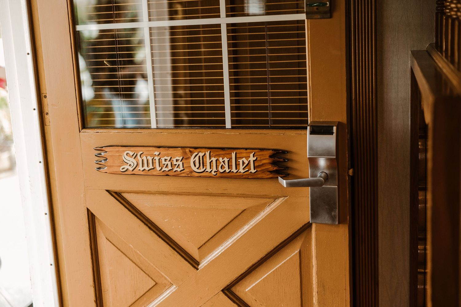 Brown wooden door with a decorative Swiss Chalet sign mounted on the panel features a cross design and metal hardware.