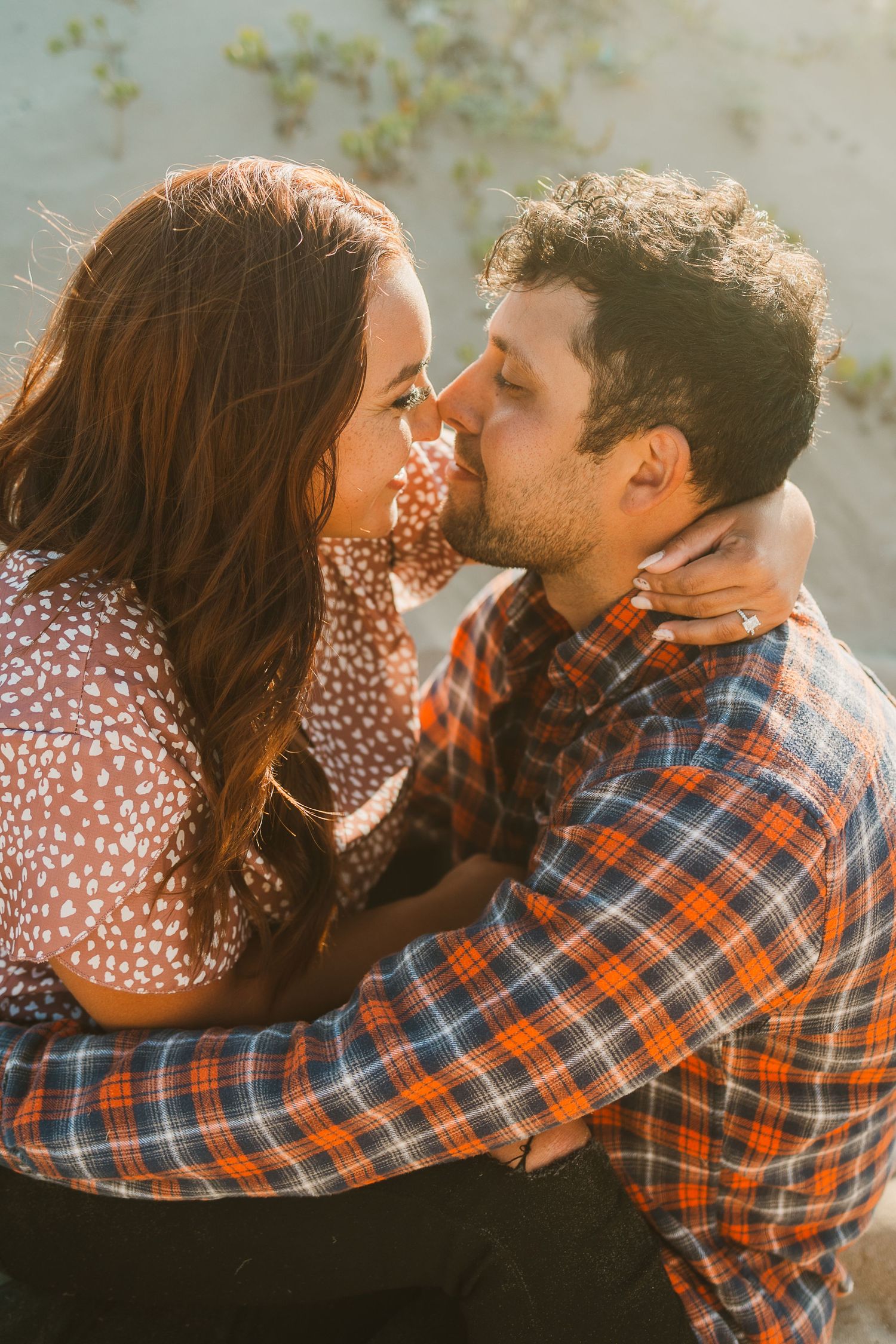 Intimate beach engagement photo of couple in coordinating casual outfits during sunset.