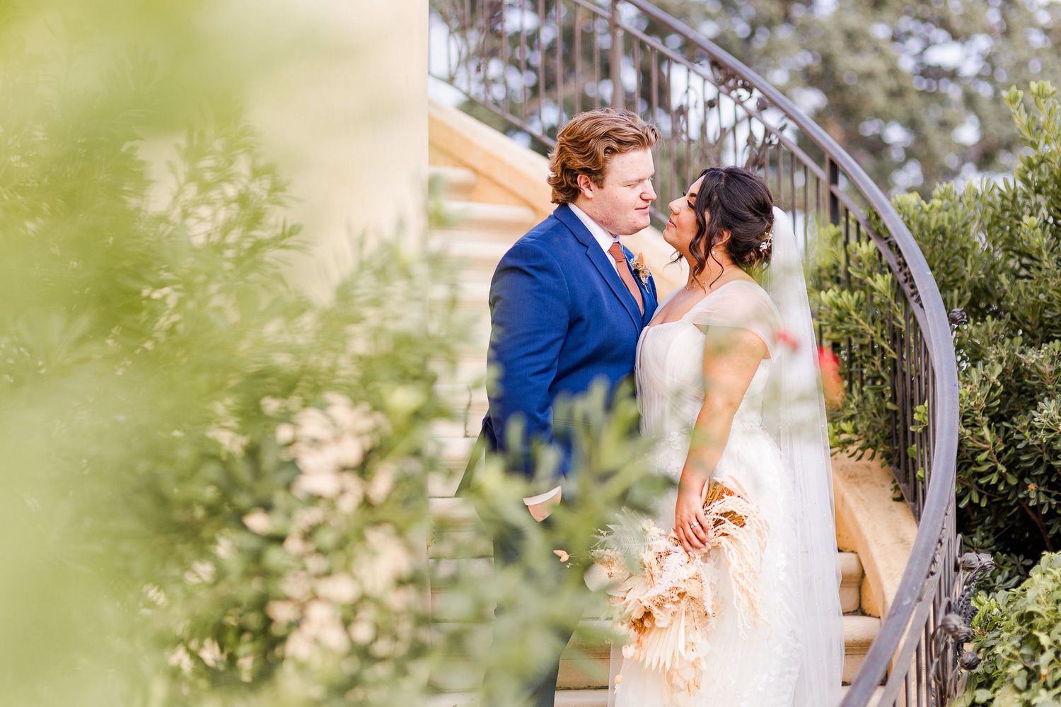 A romantic wedding portrait on curved stairs surrounded by lush garden greenery.