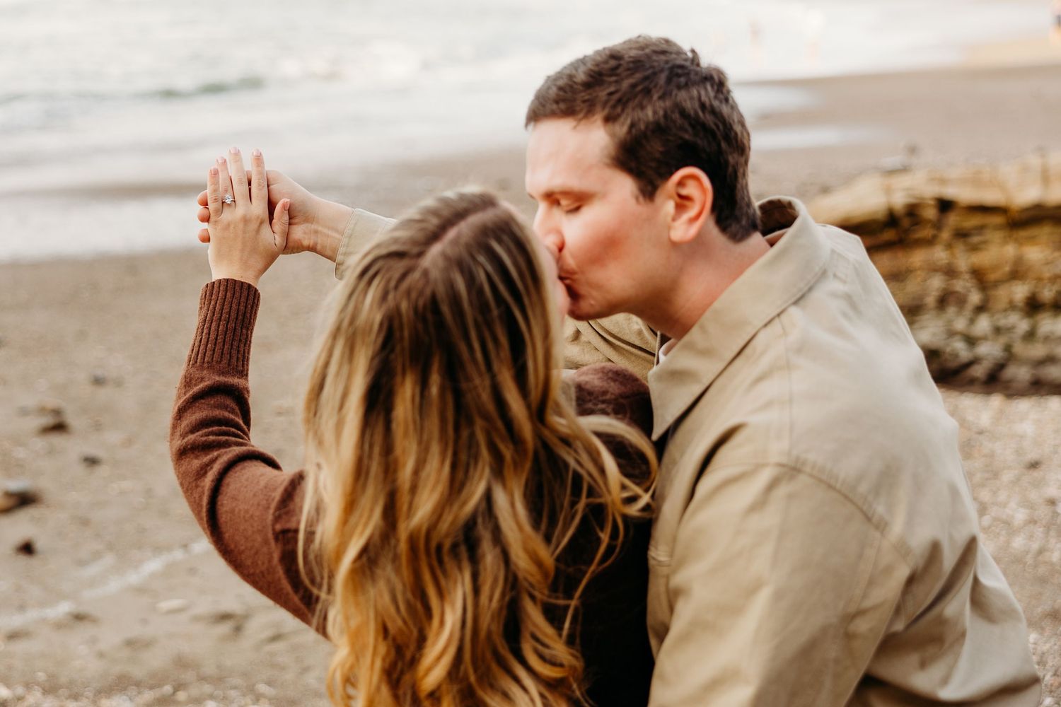 Couple embraces on a misty beach during golden hour while sharing an intimate moment together.