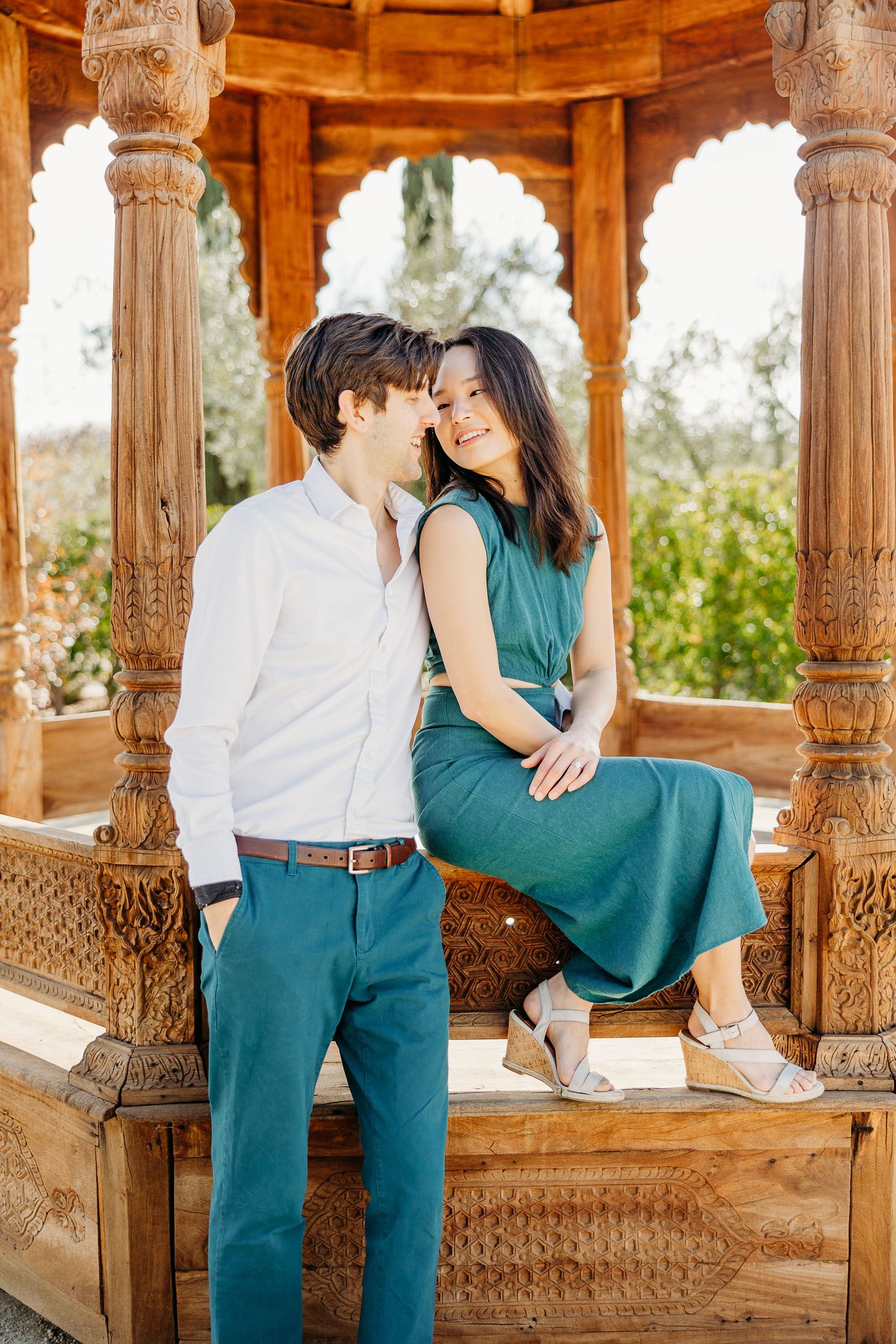 Romantic couple in coordinated outfits sharing an intimate moment in a wooden gazebo.