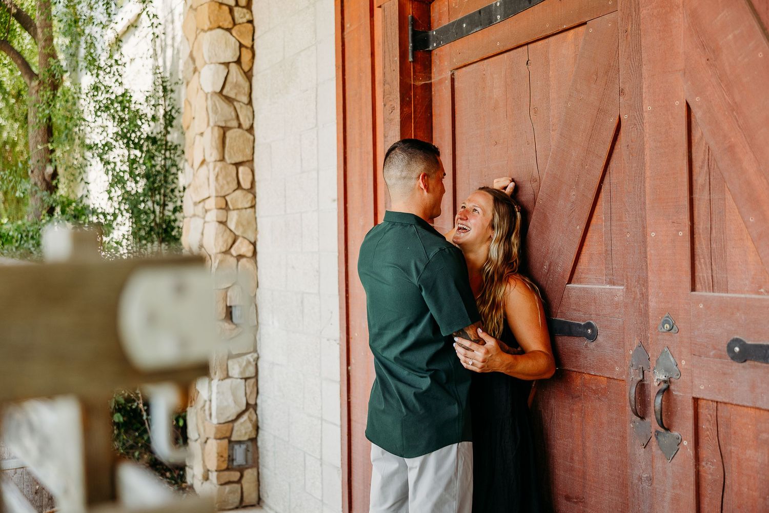 Couple sharing a romantic moment against a rustic wooden door and stone wall backdrop.