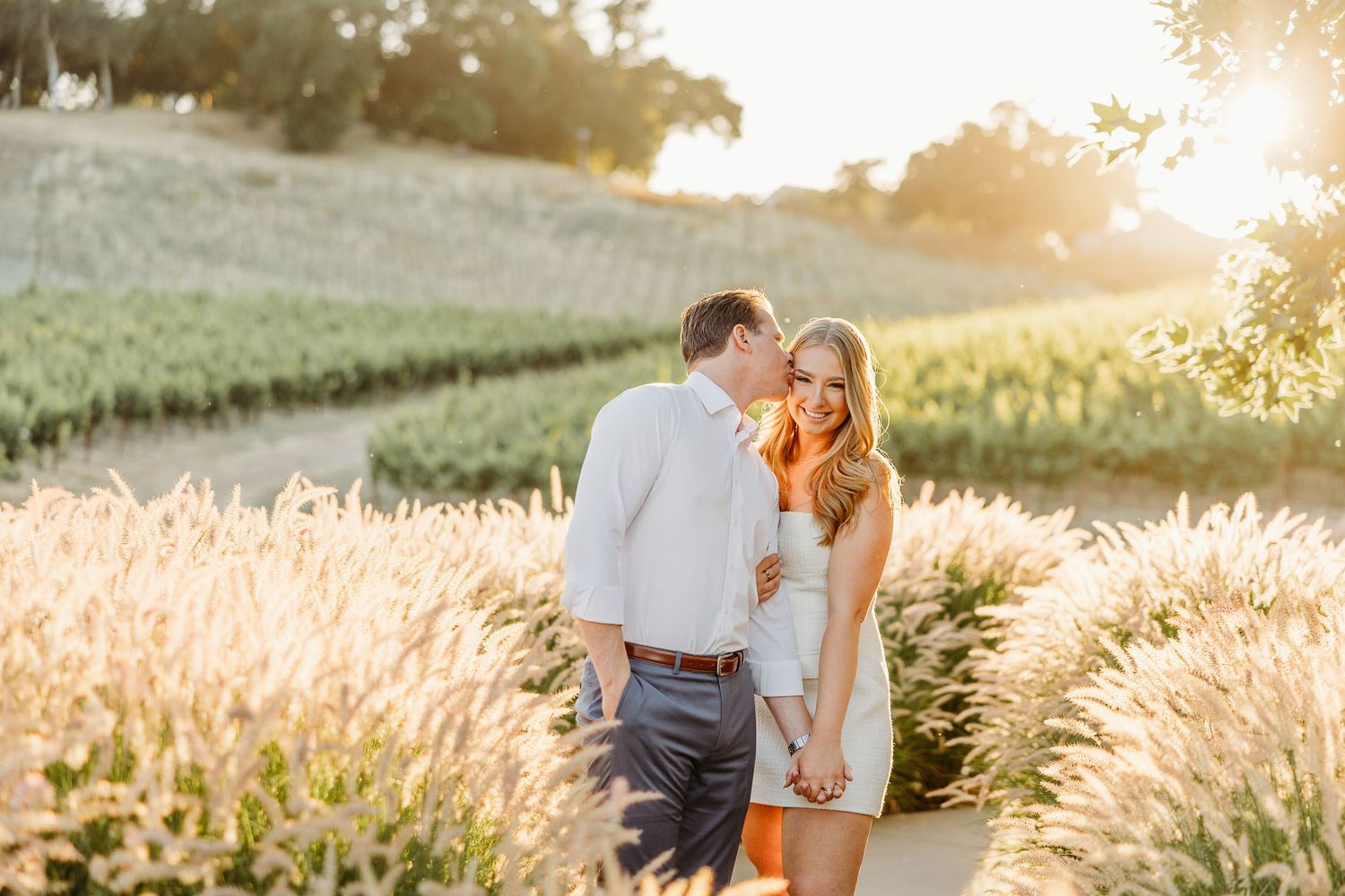 Romantic couple embraces in golden wheat field at sunset creating dreamy silhouettes against glowing sky.