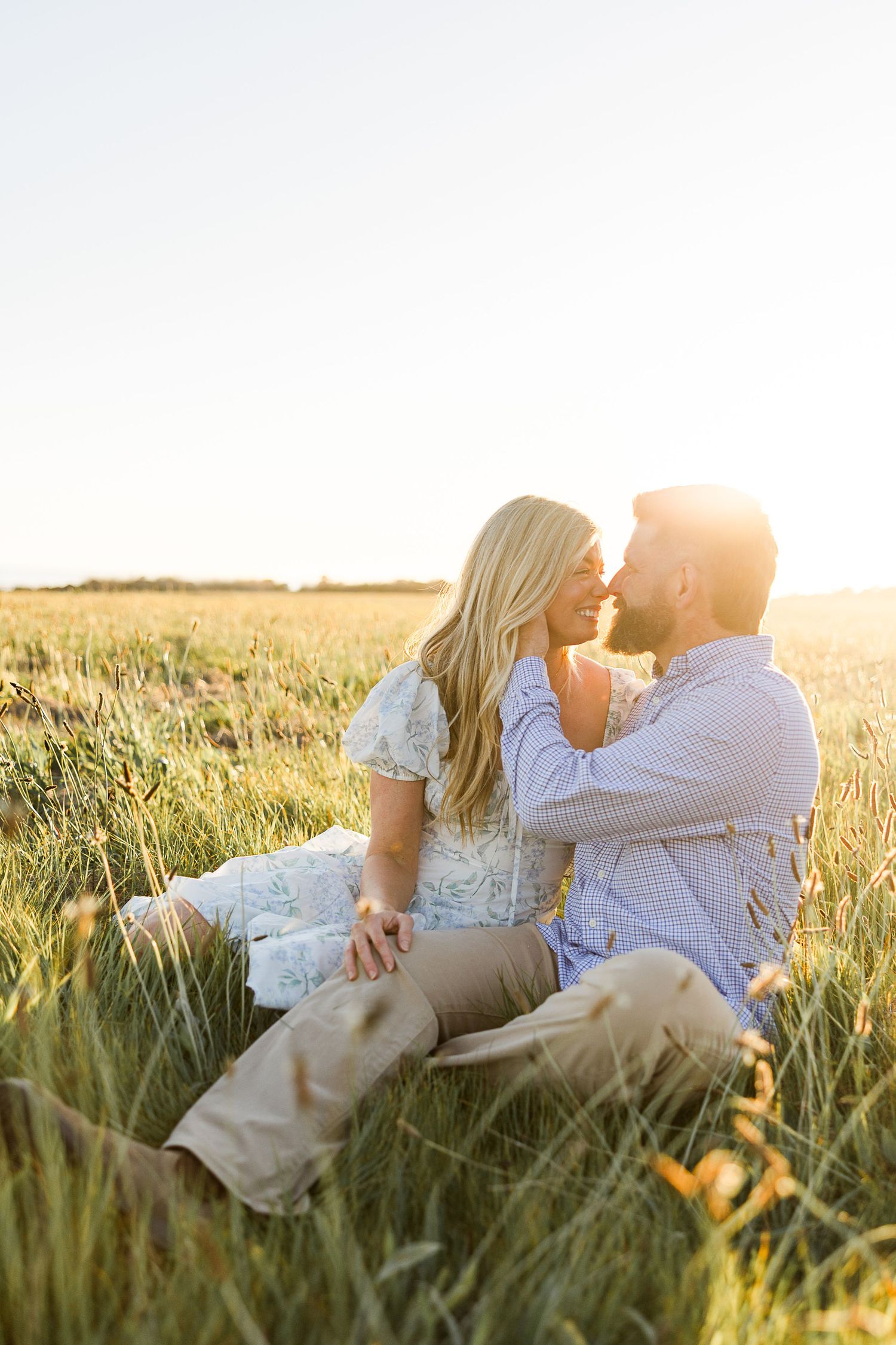 A romantic couple shares an intimate moment while sitting in a golden wheat field at sunset.