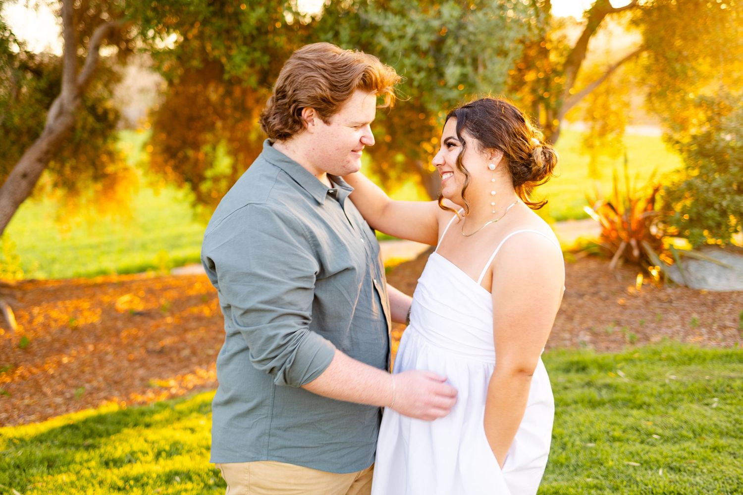 Tender moment between couple in garden with warm sunset lighting filtering through trees.